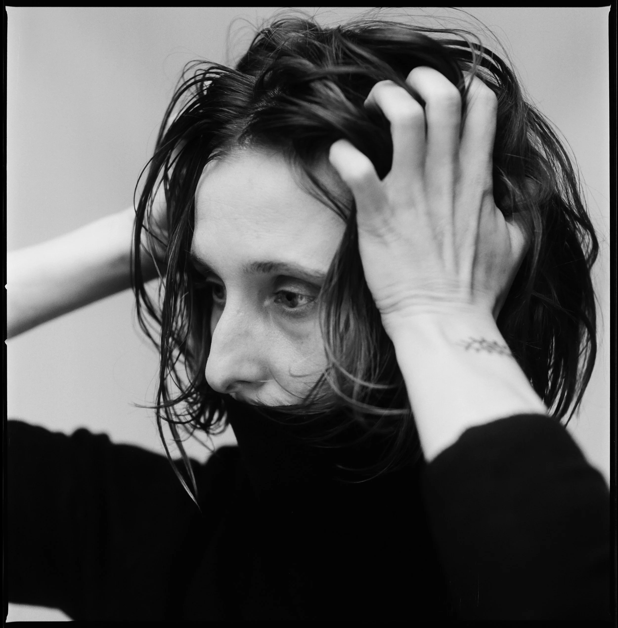 Black and white close-up portrait of a woman with messy hair, holding her head with both hands, looking down thoughtfully.