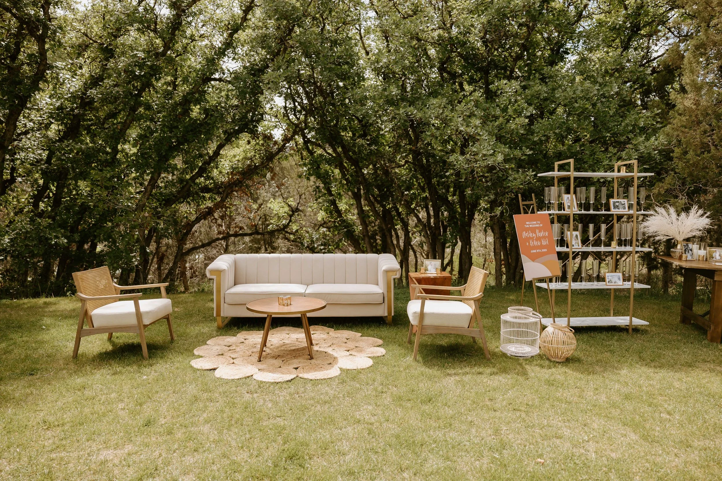 Modern outdoor wedding lounge area with cream sofa and woven chairs at Vista View Events, a Colorado mountain wedding venue, surrounded by mature trees