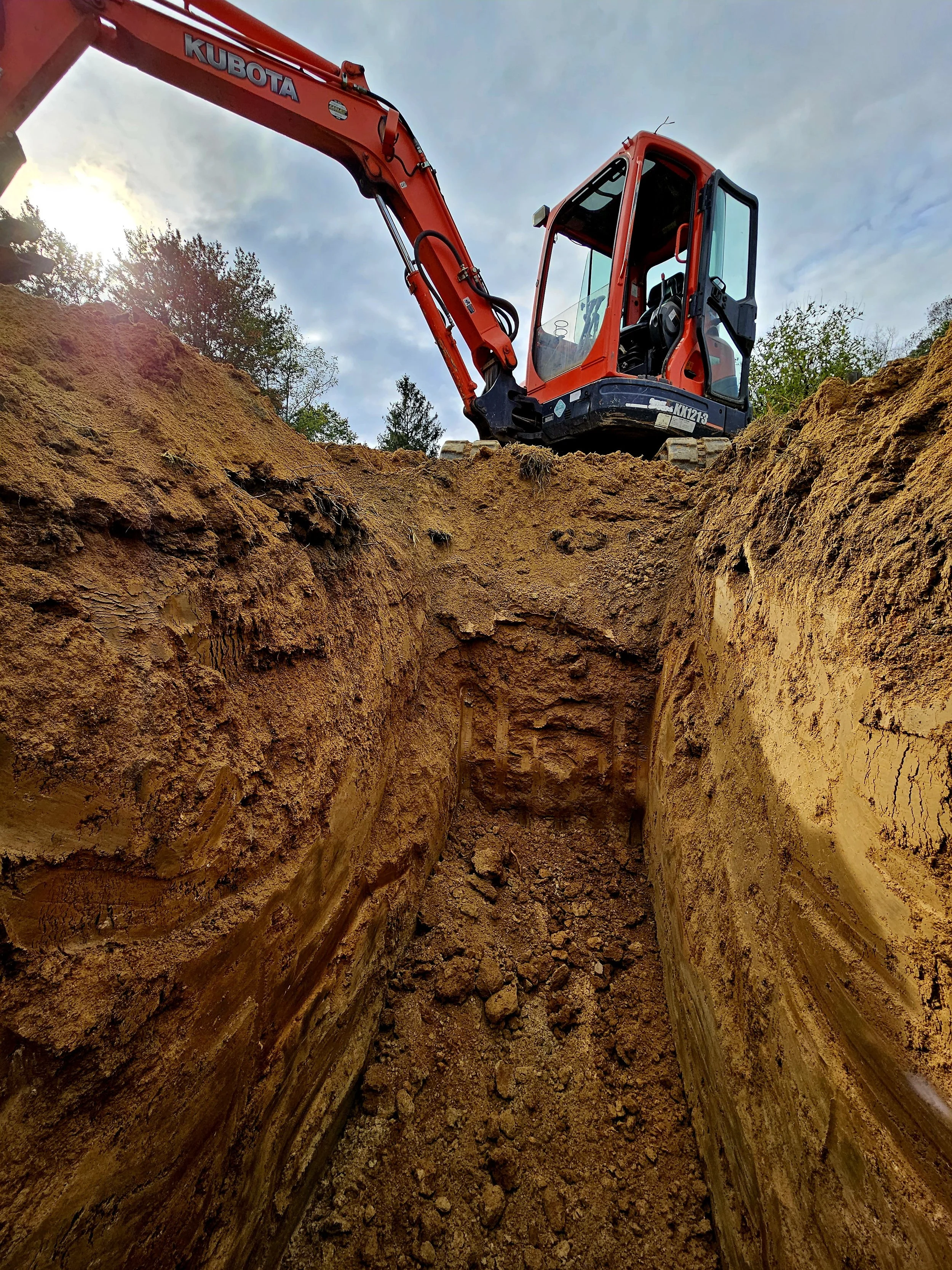 A red Kubota excavator is digging a deep trench in the ground for Septic Testing