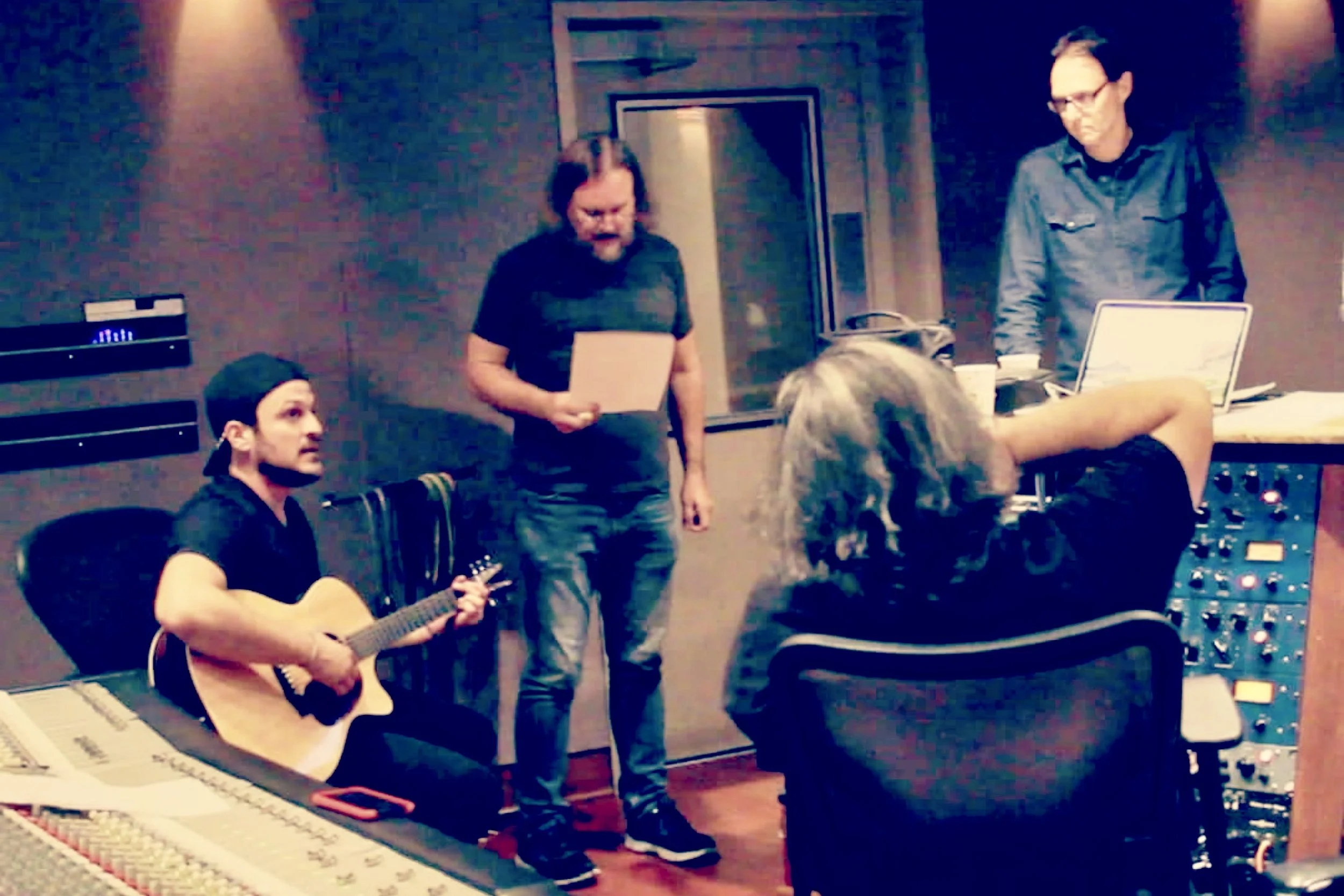 Singer-songwriter session in a Nashville recording studio capturing a collaborative production moment, featuring acoustic guitar, lyric sheets, and engineering work at a mixing console — reflecting creative partnership and intentional recording.