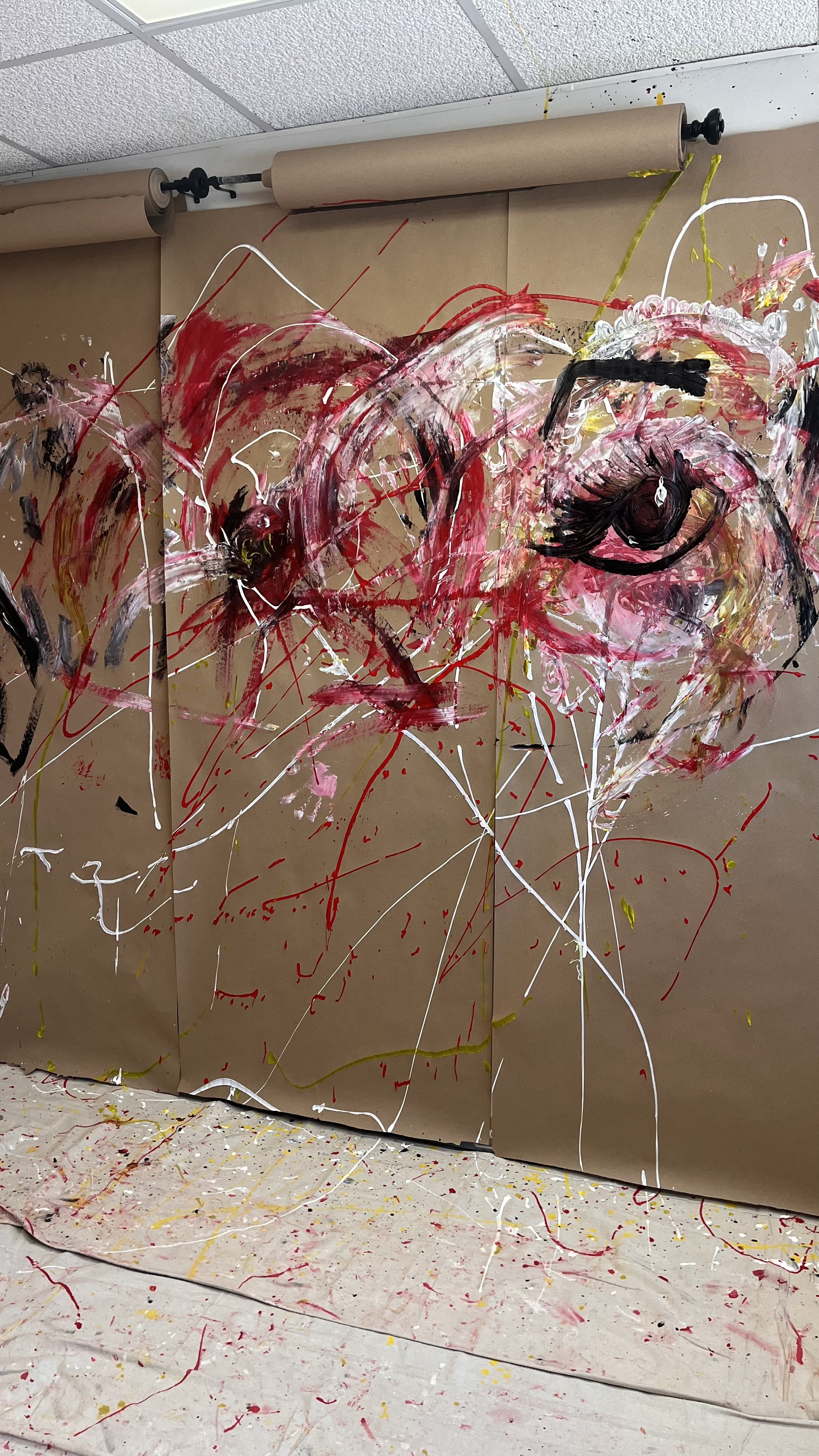 Abstract painting with large eye sketches on brown paper, featuring red, black, white, pink, and yellow paint splatters and bold strokes.