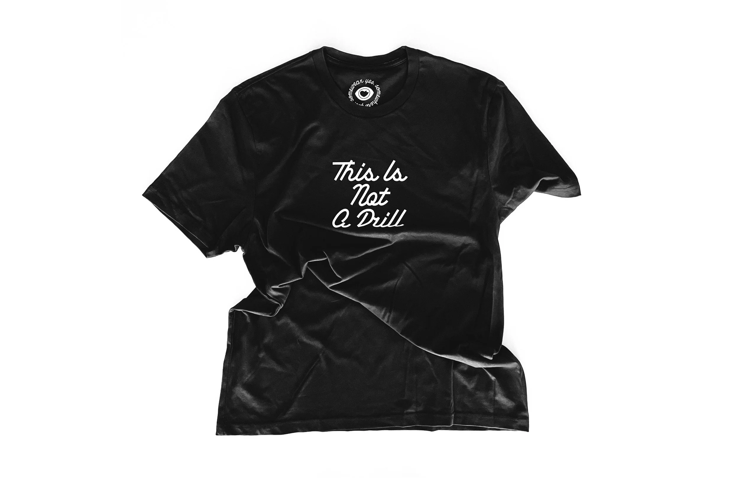 Black satin T-shirt with white text that reads 'This is Not a Drill' laid flat against a white background.