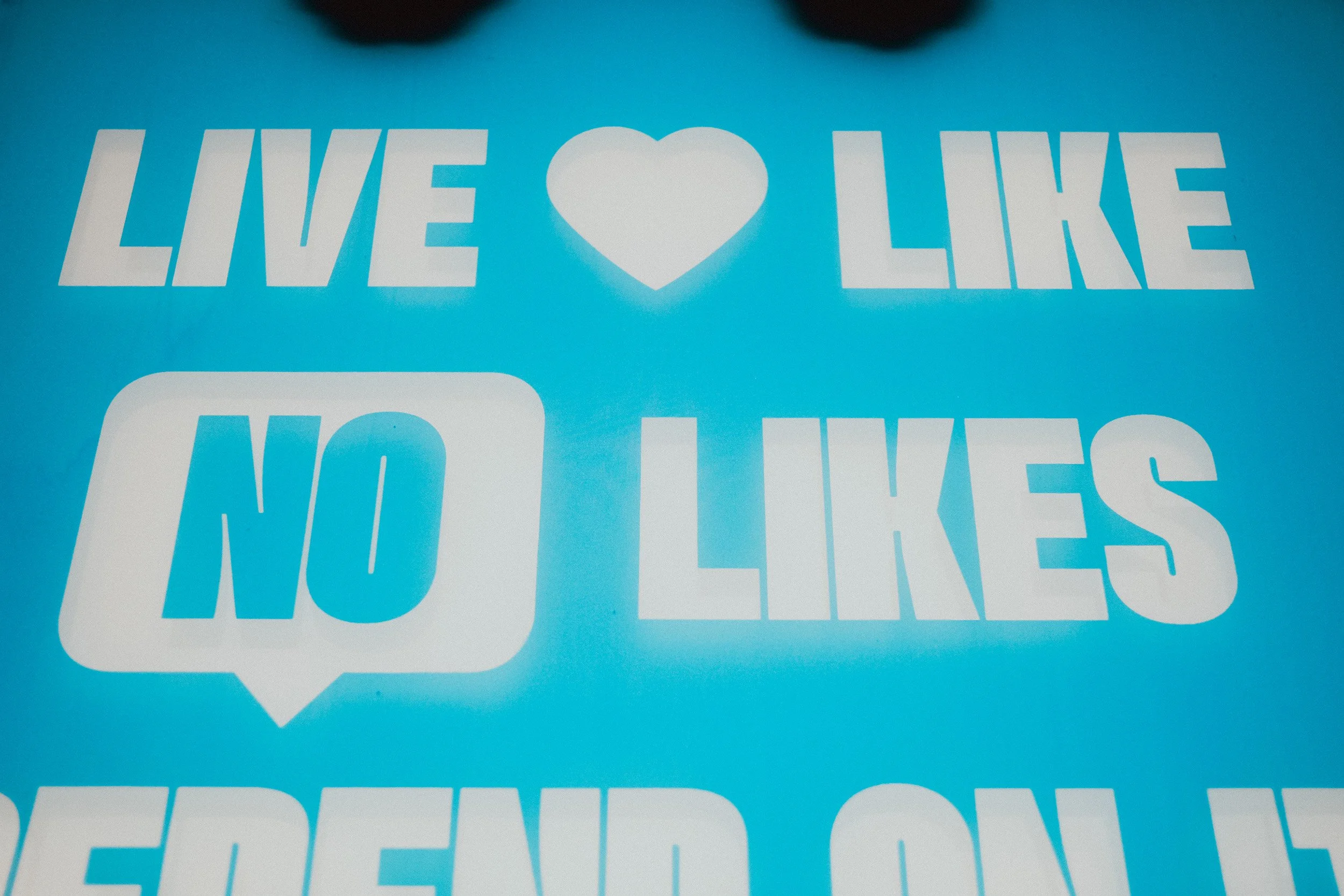 Message on a blue background reading "Live Love No Likes" with a heart icon replacing the word "love" and a speech bubble around "No".