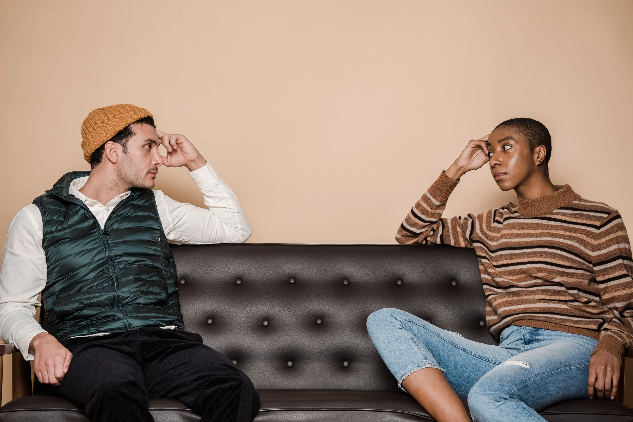 Two people sitting apart on a couch, looking toward each other with thoughtful expressions during a tense moment.