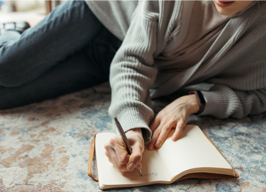 Person relaxing on a rug while writing in an open journal, practicing quiet reflection in a cozy home setting.