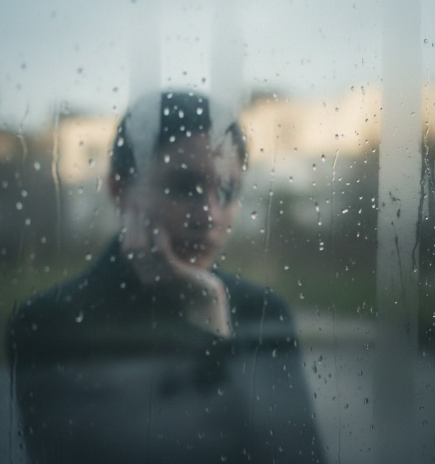 A blurred reflection in glass, with indistinct features and a quiet, contemplative mood.