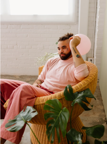 Person sitting thoughtfully in a chair at home surrounded by plants.
