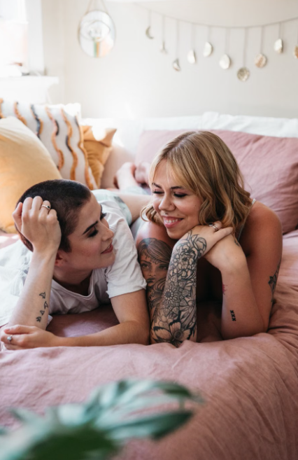 Two people relaxing together on a bed and smiling, representing comfort and connection in relationships.
