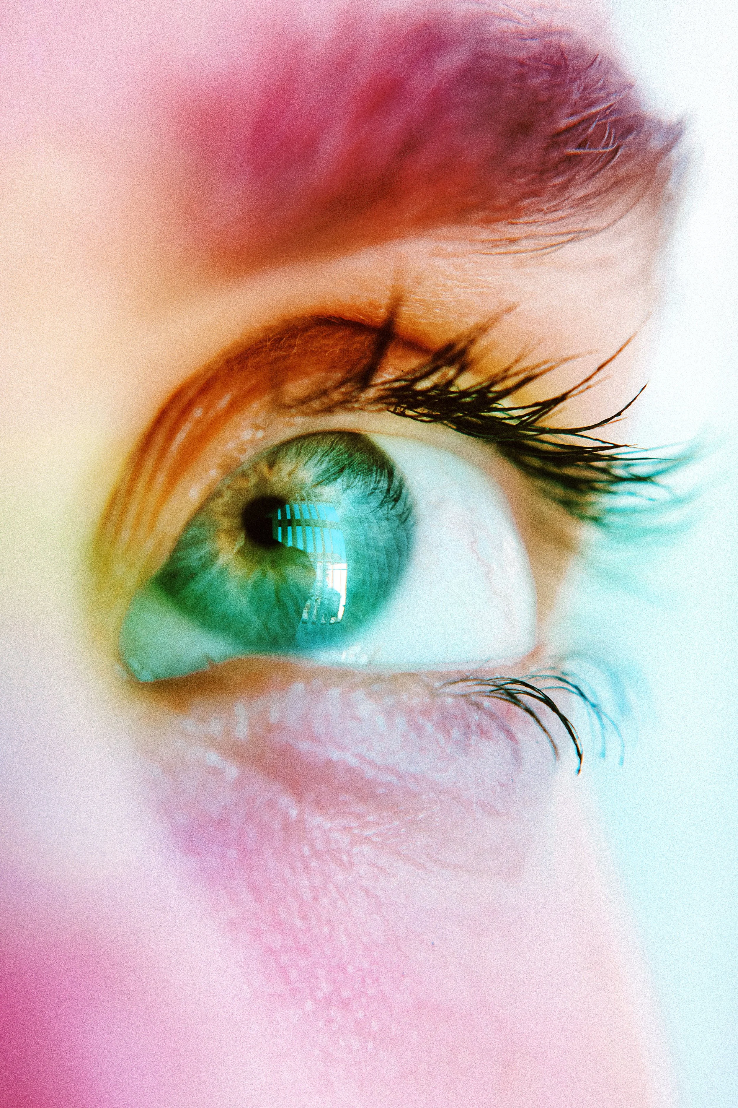 Close-up of an eye illuminated by soft pink, teal, and warm-colored light.