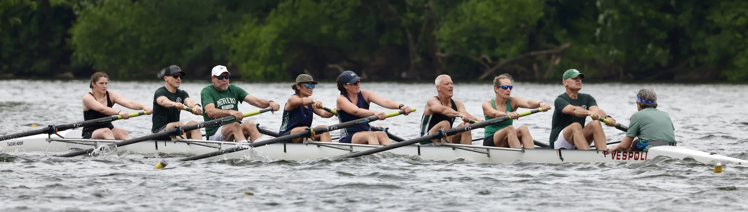 A rowing team of nine people rowing a boat on a lake, with a person sitting at the front steering and giving commands.