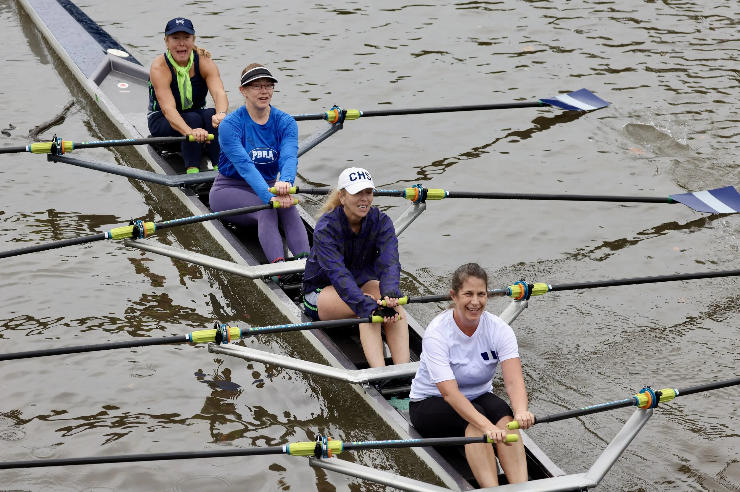 Four women rowing a boat on a body of water during daytime, smiling and enjoying the activity.