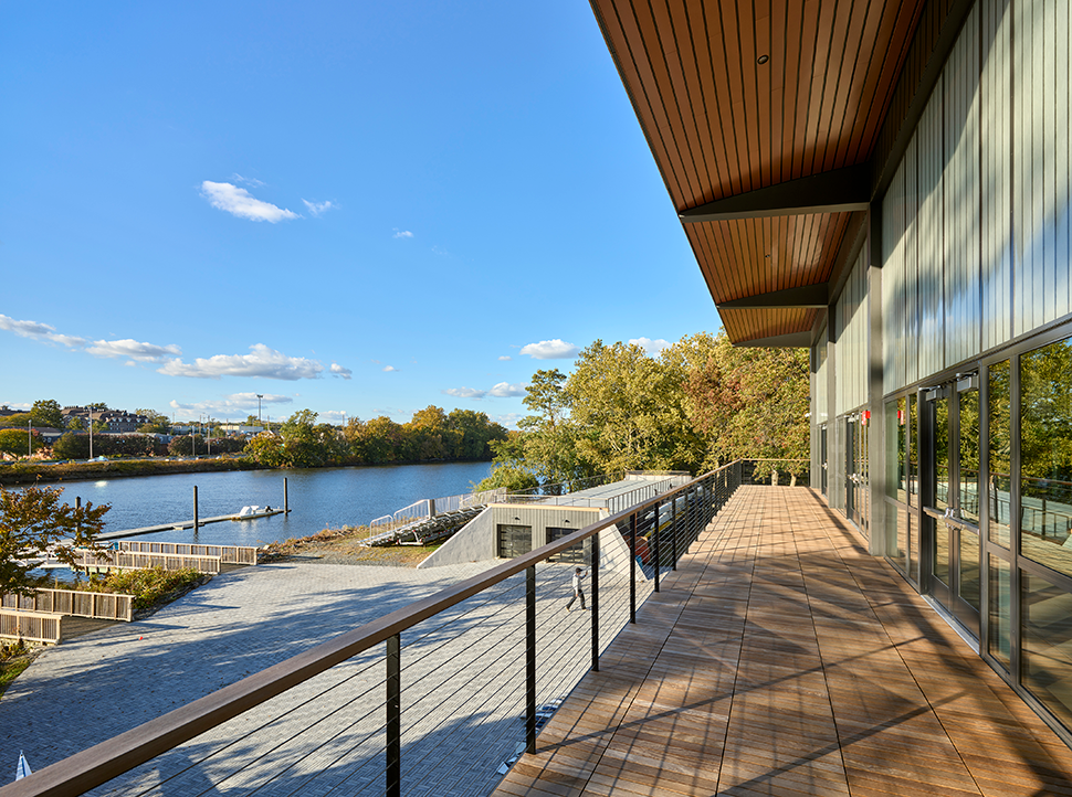 A spacious balcony with a metal railing, overlooking a river with trees and a clear blue sky.