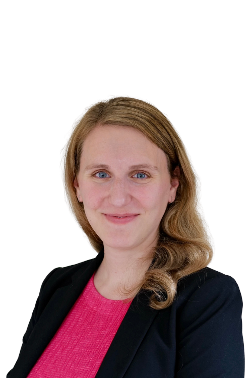 A woman with shoulder-length red hair, wearing a black blazer over a pink top, smiling at the camera against a white background.