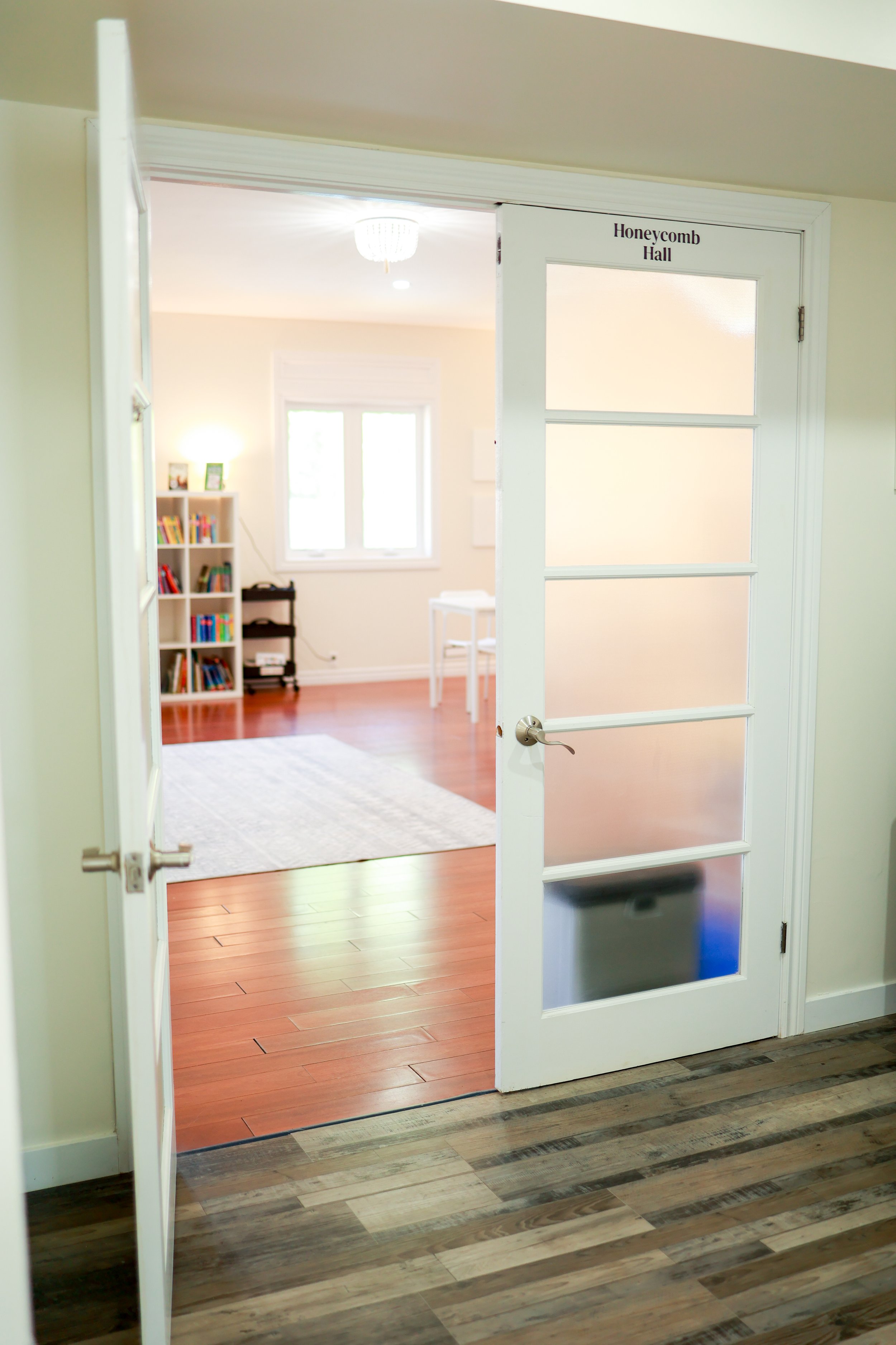 Open door labeled 'Honeycomb Hall' leading into a bright room with a window, bookshelf, and white table.