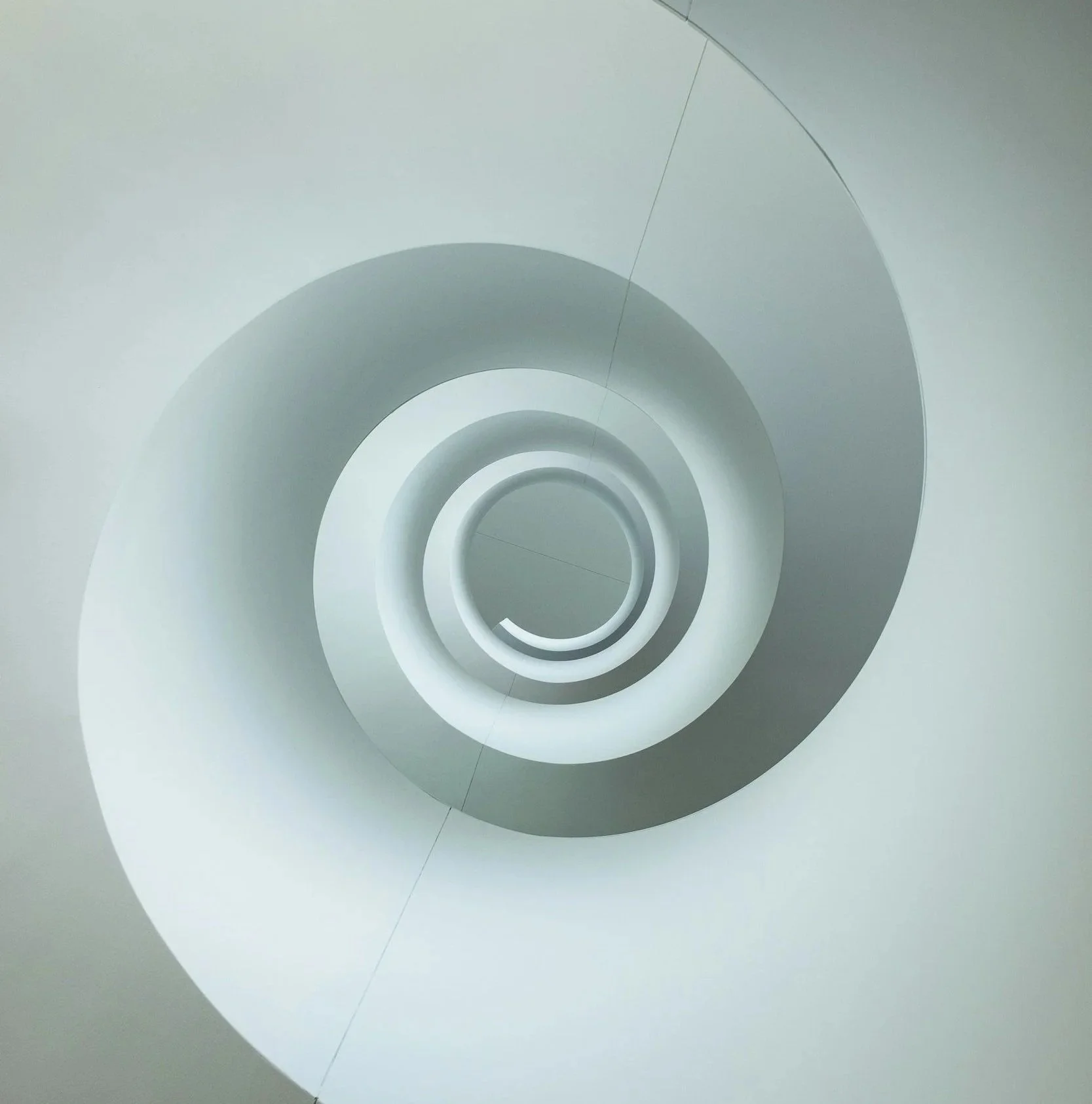 Looking up a spiral staircase from the bottom, showing the concentric circular steps and smooth white walls.