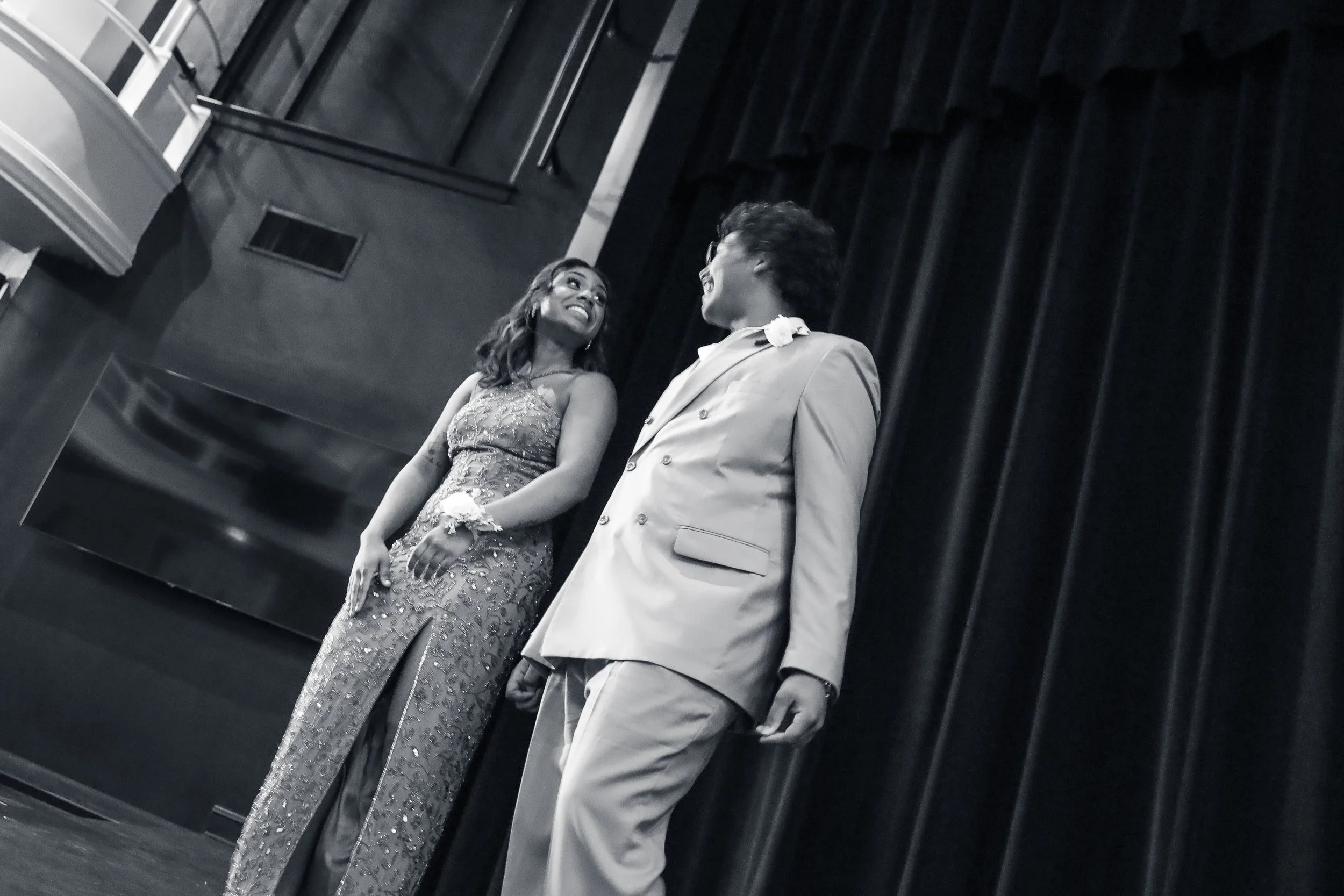Two women dressed in formal attire standing and smiling, near a dark stage curtain.