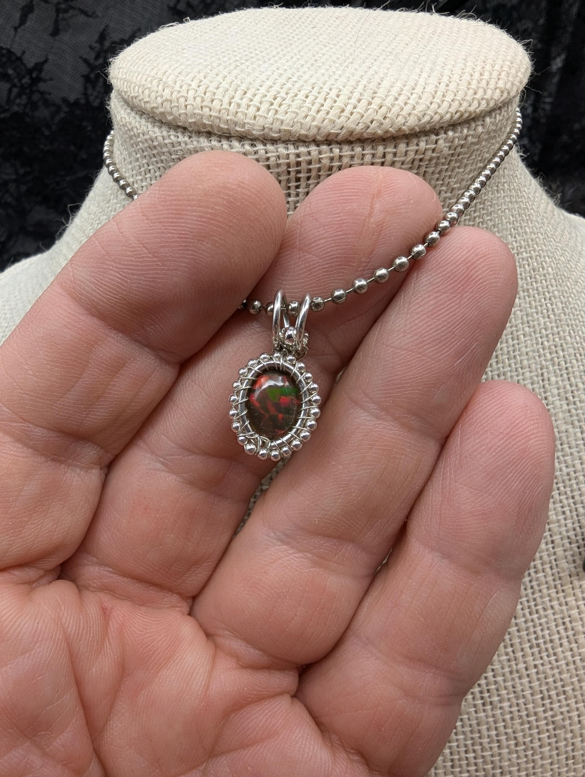 Discover this exquisite Ethiopian black opal sterling wire-wrapped pendant, elegantly accented with shimmering silver beads, showcasing a dazzling spectrum of colors.