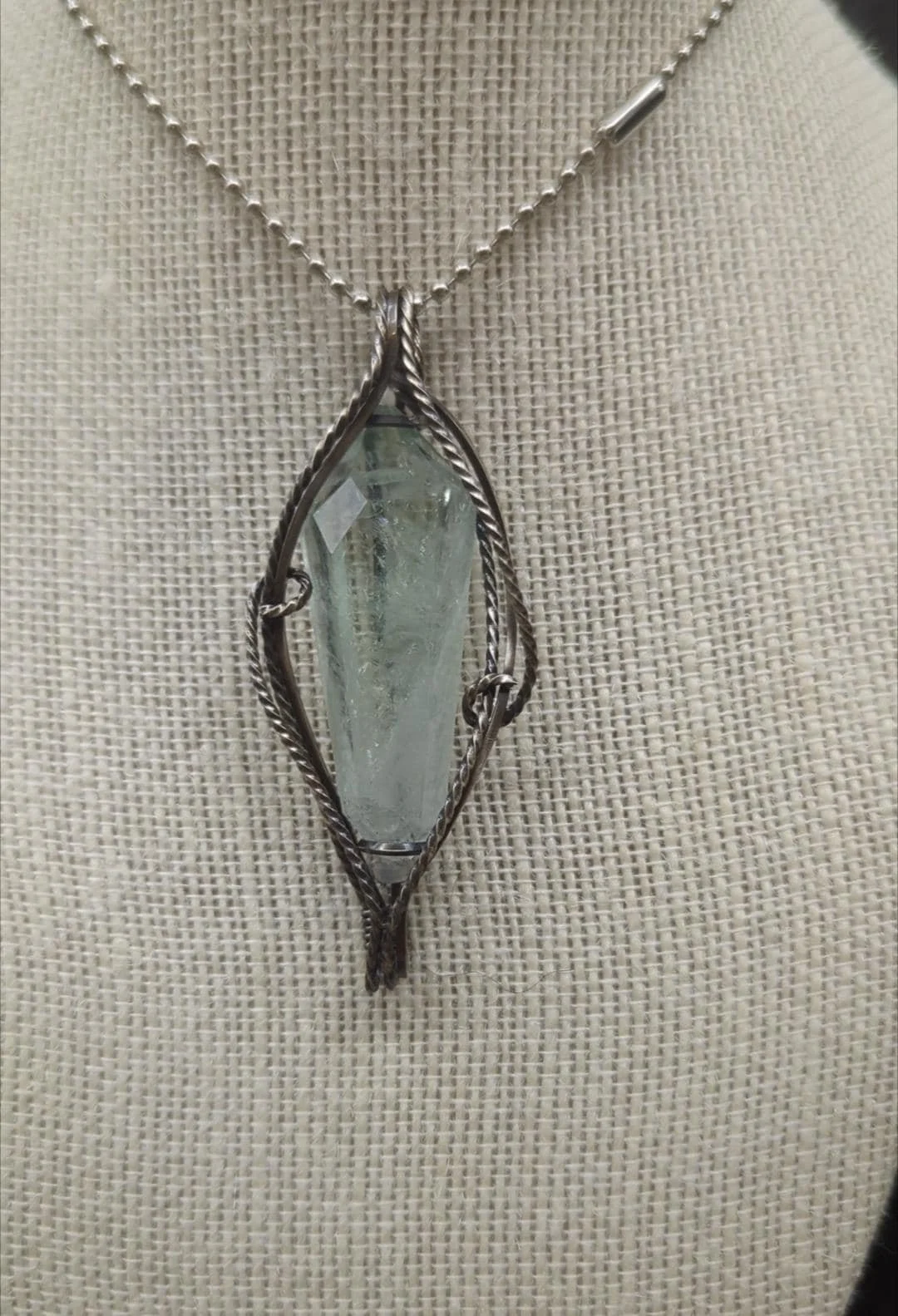 A pristine double-terminated green quartz prasiolite point elegantly wrapped in solid antiqued copper wire, cascading along both sides with kitty-corner swirls.