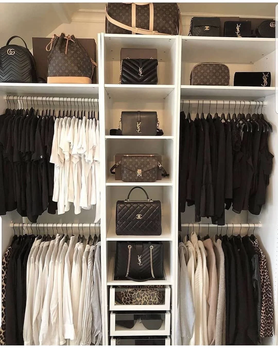 Closet organized with luxury handbags, wallets, and clothing. Brands include Louis Vuitton, Chanel, and Yves Saint Laurent. Clothes are neatly arranged on hangers, divided into white and black sections.