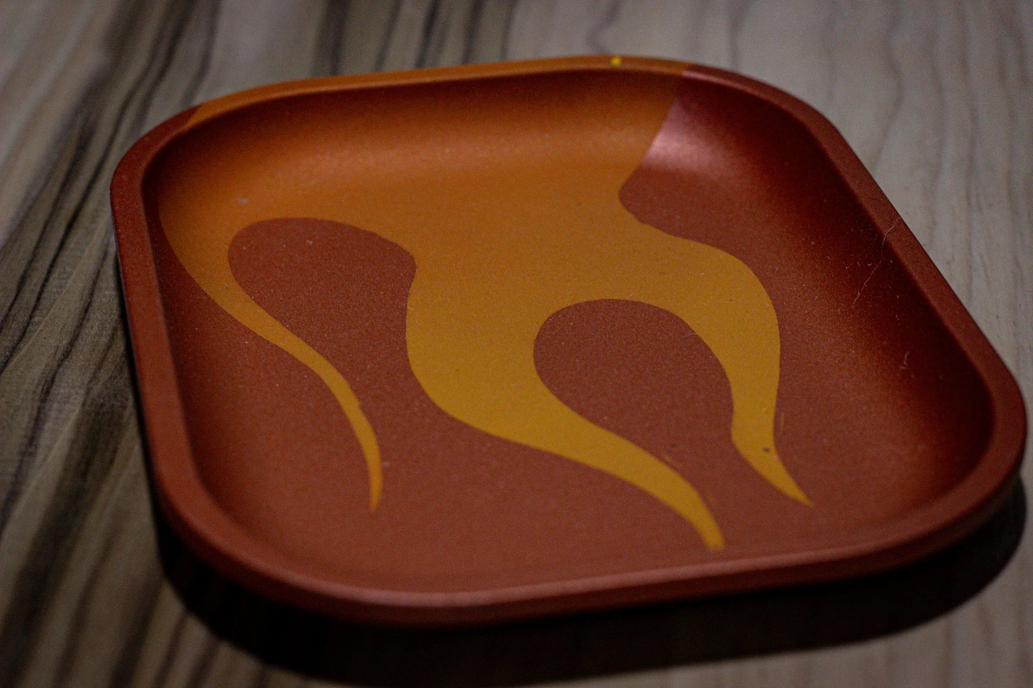 A close-up of an orange rectangular tray with a yellow and orange flame design on the inside, placed on a wooden surface.
