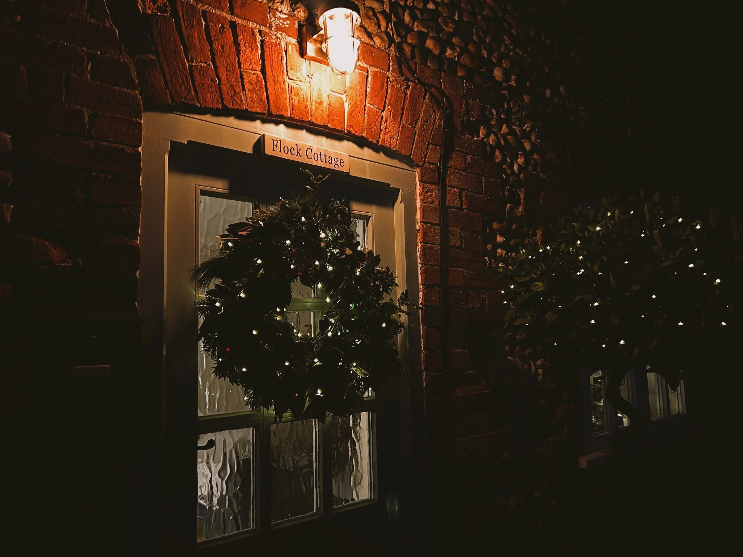 brick and flint cottage with a large thistle and holly real wreath with warm glow fairy lights. Hunstanton Norfolk 