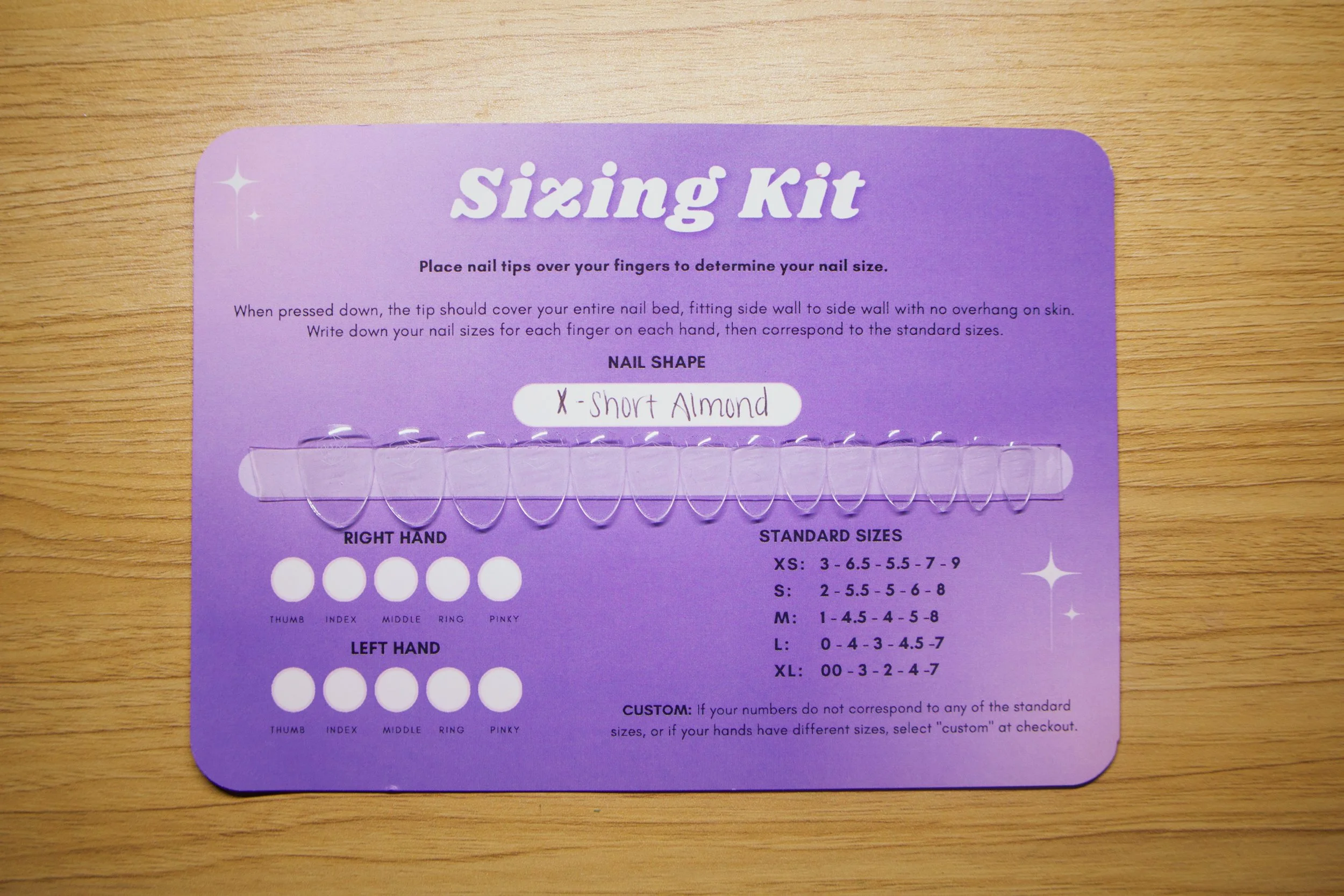 A purple nail sizing kit card with instructions and ring sizes, featuring white dots for finger size measurement and a label indicating 'X - Short Almond' nail shape.