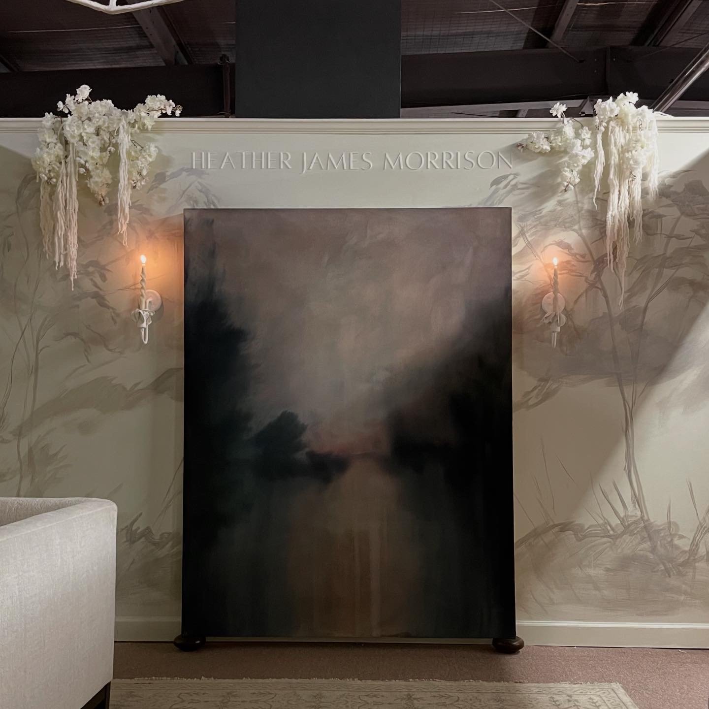 Wall decorated with white floral arrangements and shears, with the name 'Heather James Morrison' displayed at the top. Sconces with lit candles are on either side of a dark painting or panel.