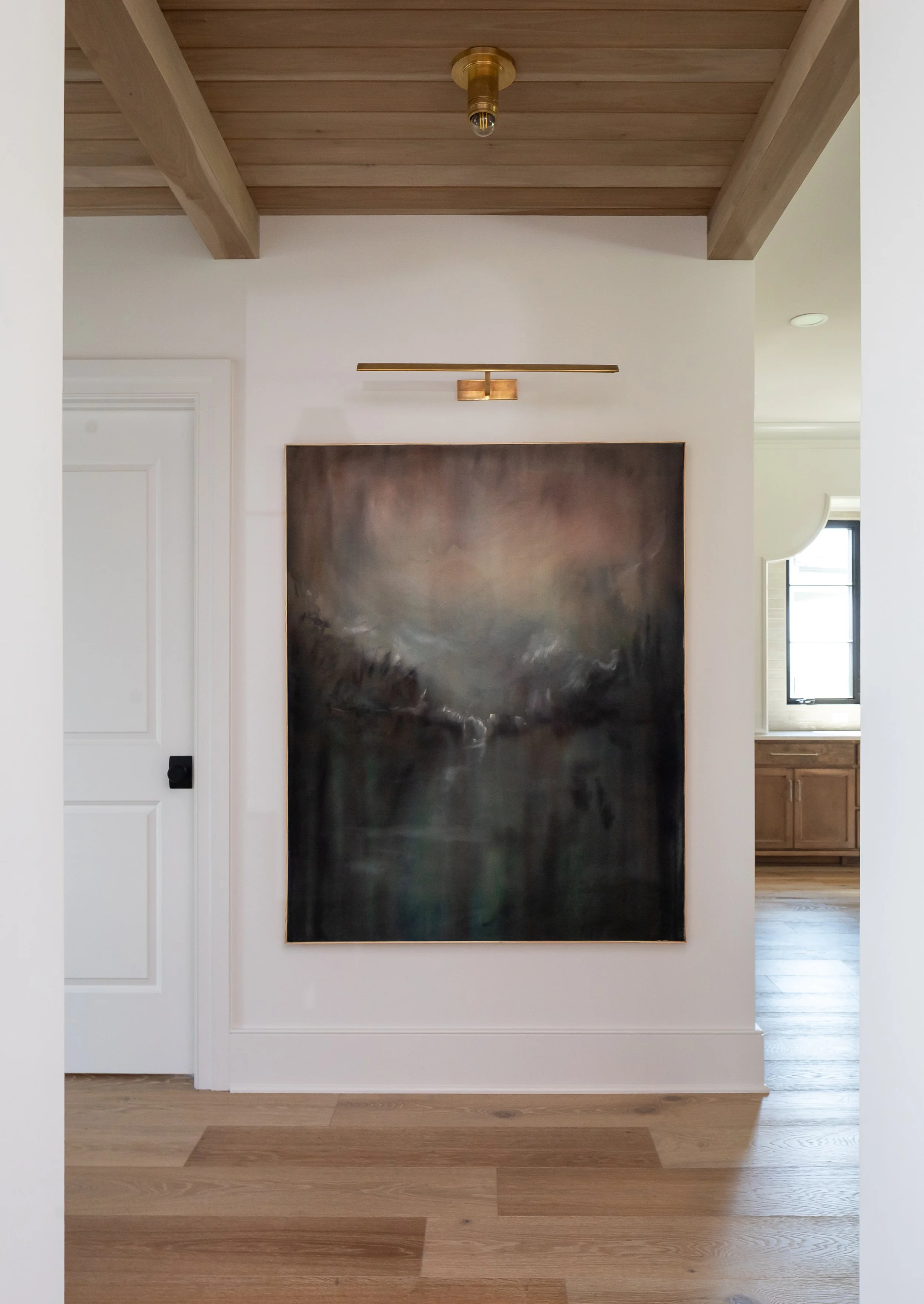 Empty white wall with a large abstract painting, wood floor, ceiling with exposed beams, and a wall-mounted light fixture.