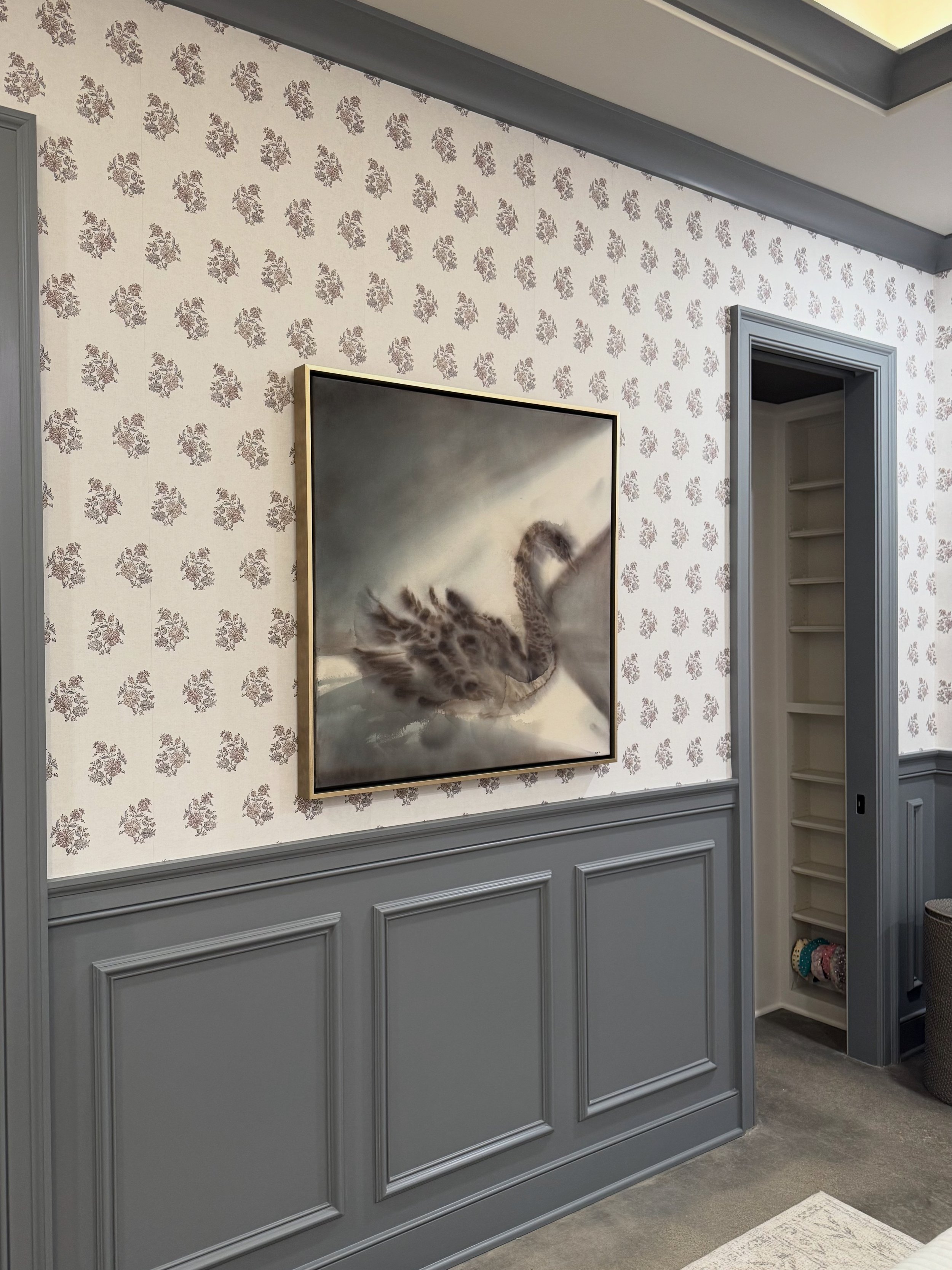 A decorative interior wall with blue wainscoting, floral wallpaper, a framed animal artwork, and built-in shelves.