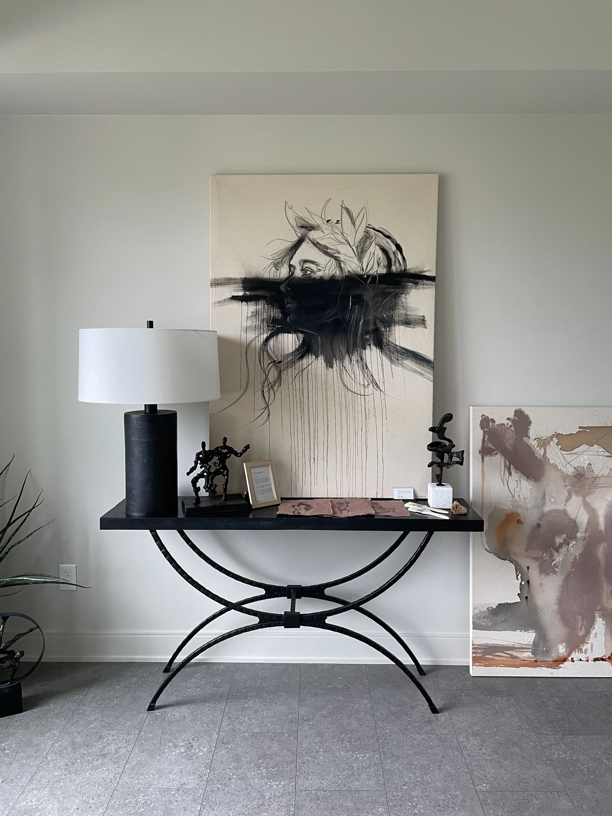 Interior of an art gallery with abstract paintings and sculptures, a black table with artistic objects and a large black and white portrait on the wall.