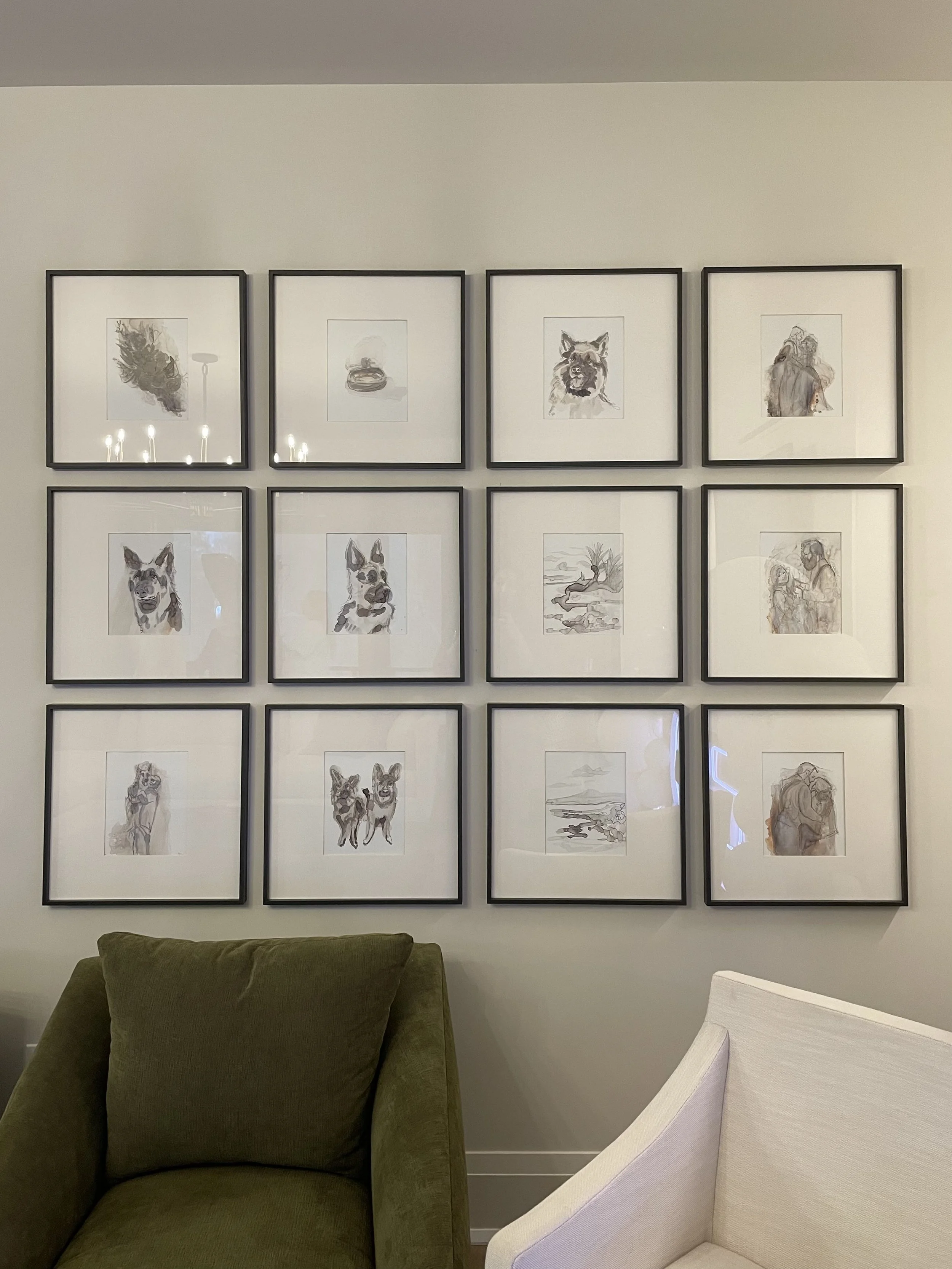 A wall with nine framed sketches of dogs, arranged in a 3x3 grid. Two armchairs, one green and one white, are in front of the wall.