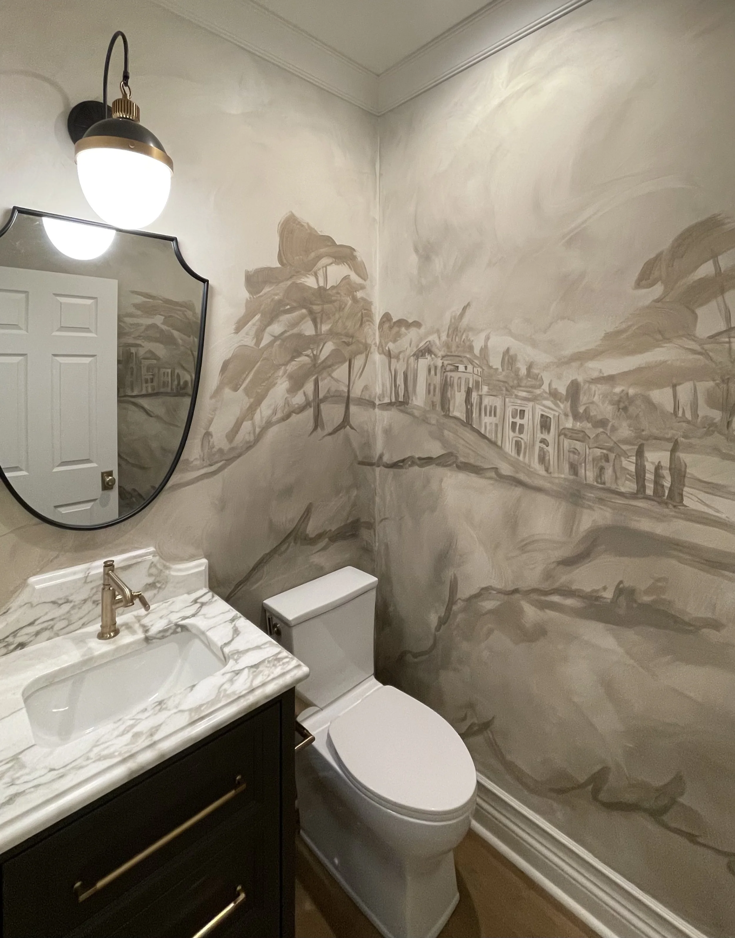 A small bathroom with a painting on the wall, a mirror, a marble countertop with a sink, a cabinet below, a toilet, and a wall-mounted light fixture.