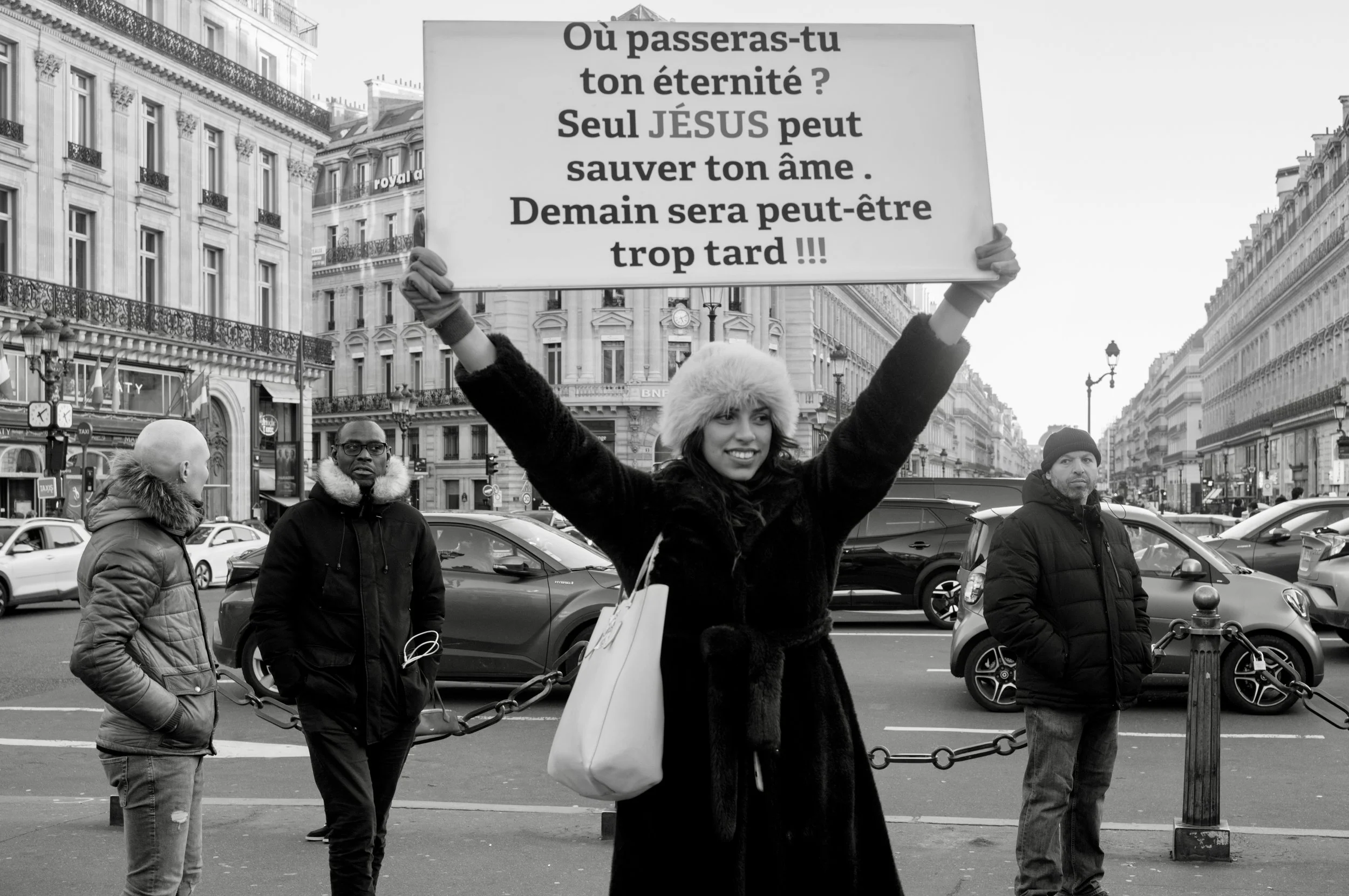 A woman holding a religious sign while preaching on a busy Paris street, photographed in black and white during a spontaneous street photography walk.