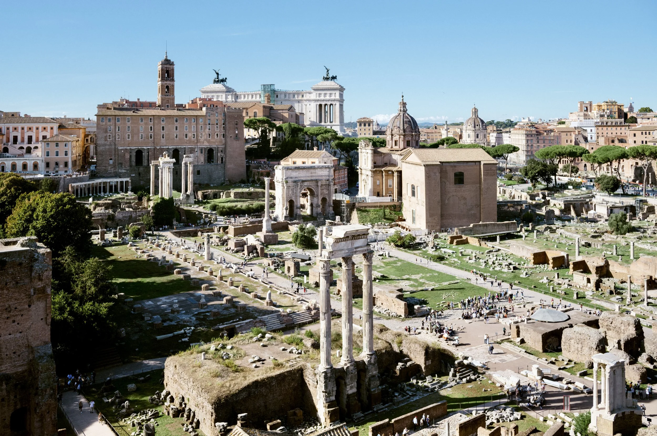 Marble columns and temple ruins in the Roman Forum with visitors exploring the archaeological site on a sunny day