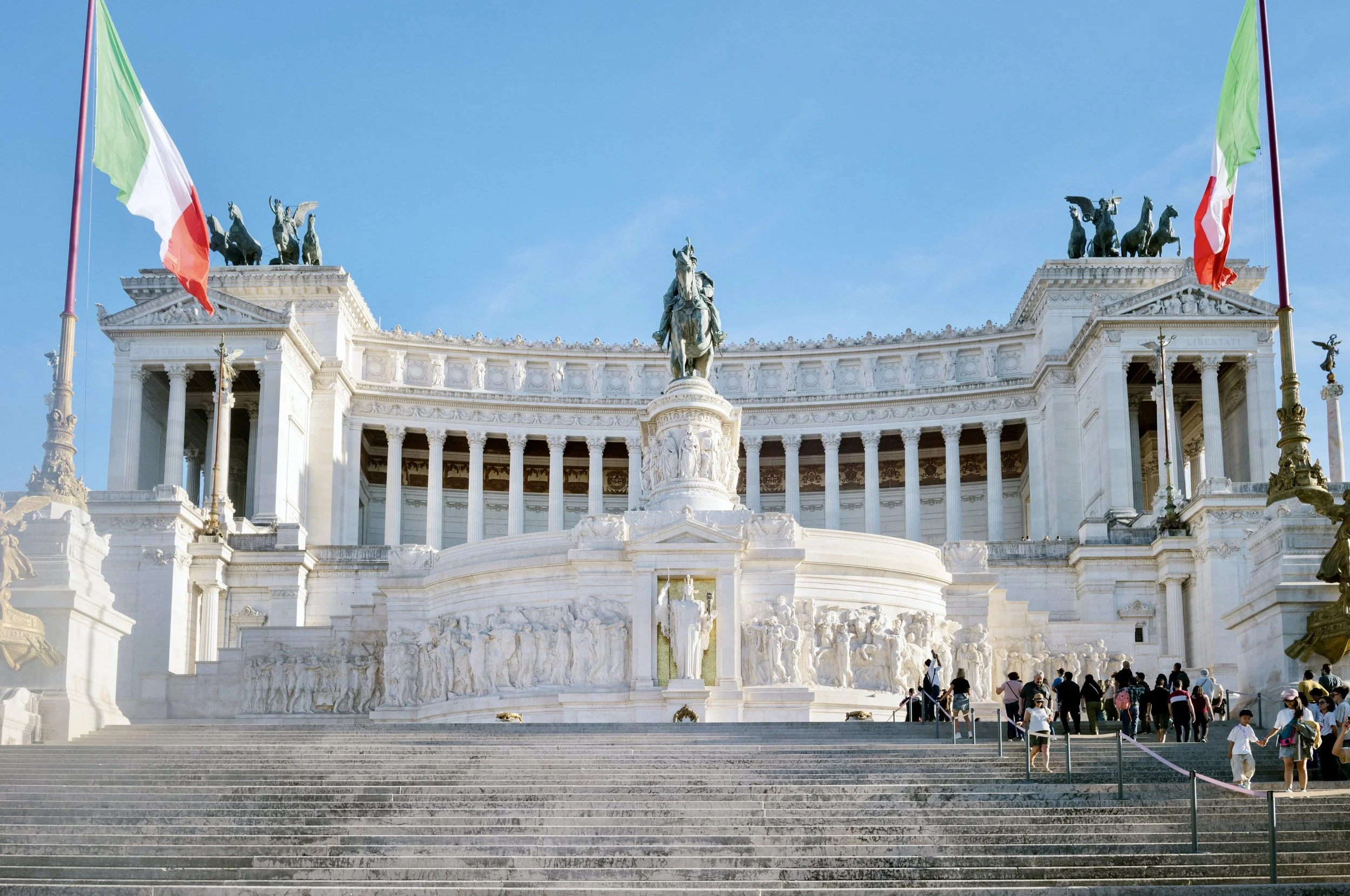 The Victor Emmanuel II Monument in central Rome, Italy, with marble façade and Italian flags under bright blue sky