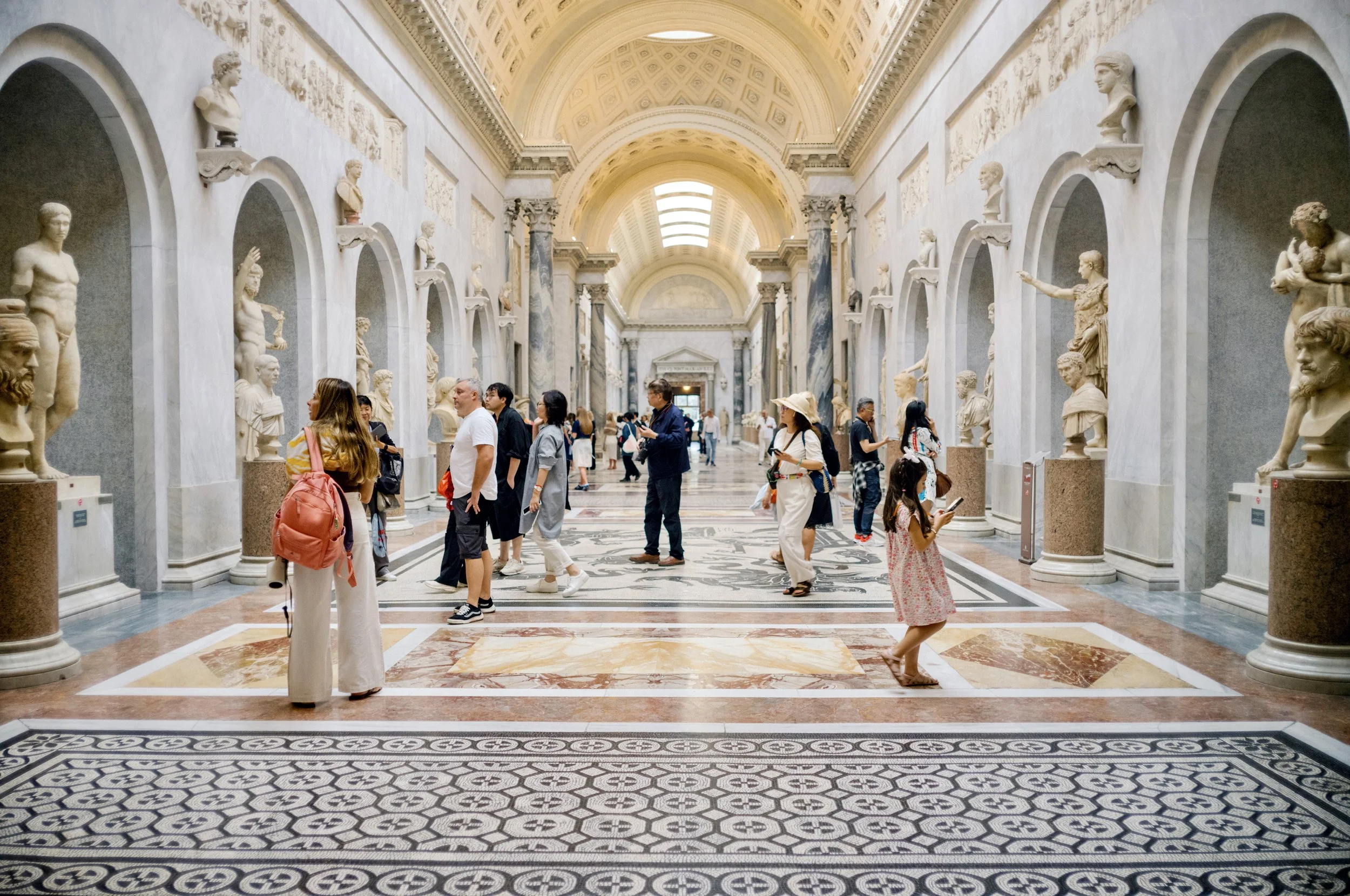 Visitors walking through the Braccio Nuovo wing of the Vatican Museums with ancient statues.