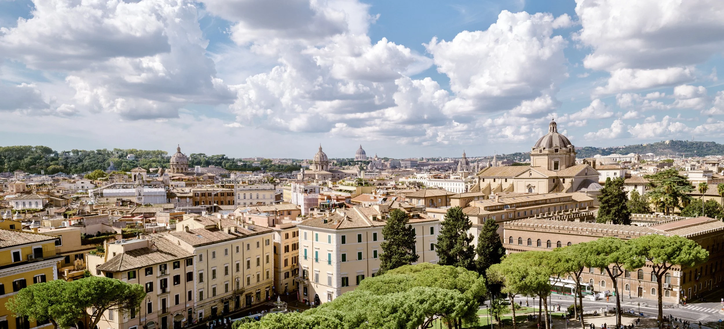Panoramic skyline of Rome seen from Palatine Hill, capturing domes, rooftops, and layered historic architecture in warm evening light.