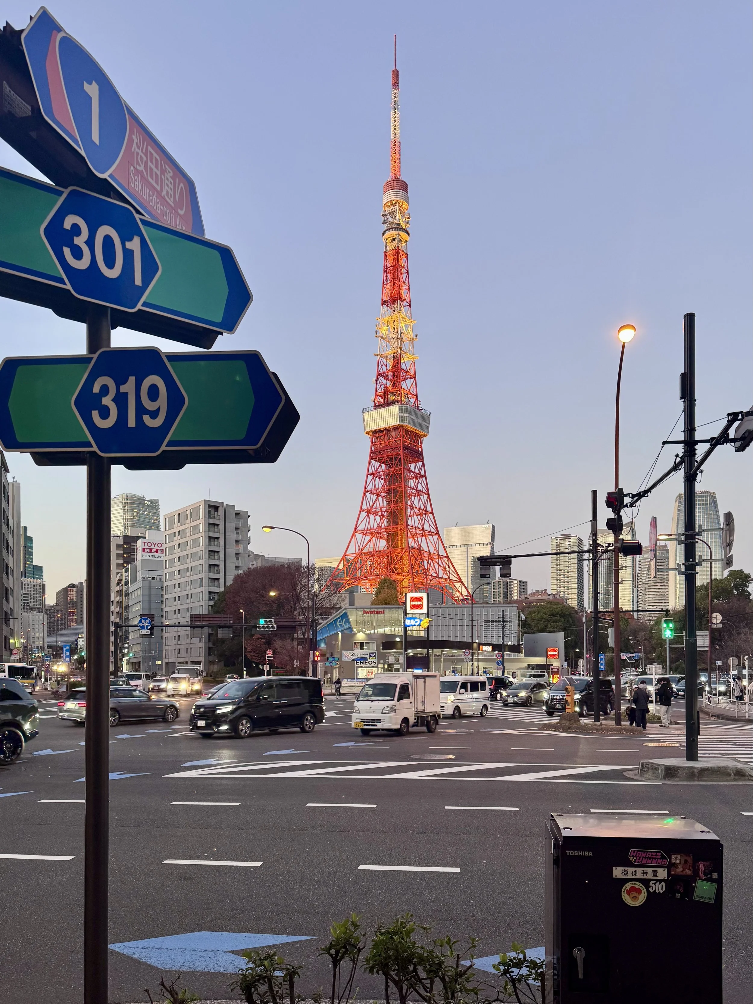 Tokyo Tower glowing at dusk above busy city streets and road signs in central Tokyo.