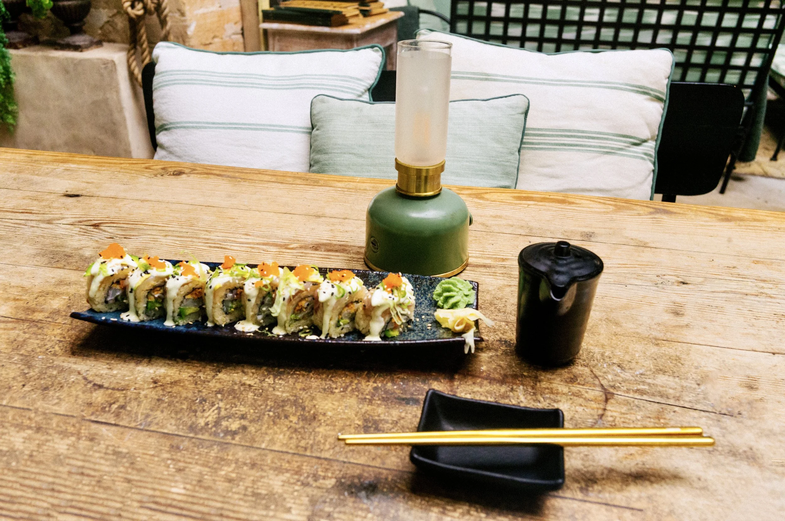 A long plate of topped sushi rolls with gold chopsticks and a lantern at a Mallorca restaurant