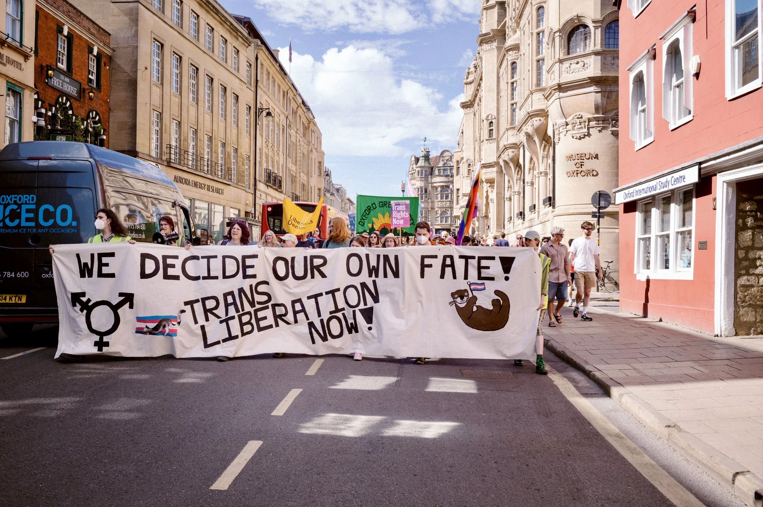 Protest march with a large banner moving down a street in Oxford city centre past the Museum of Oxford