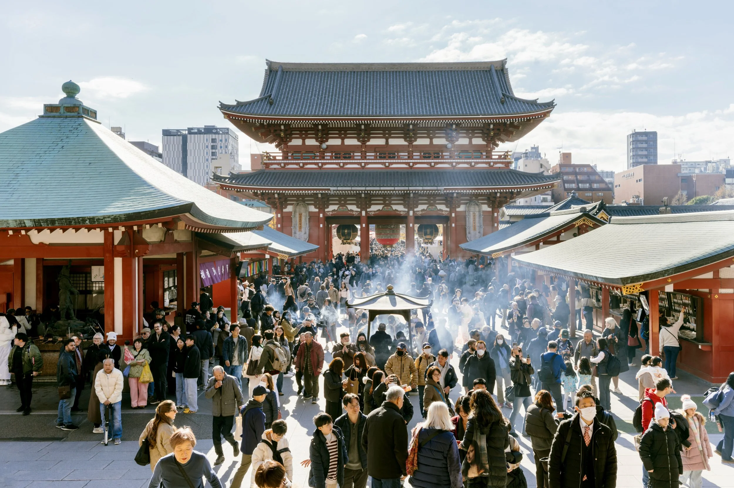 Busy courtyard scene at Sensō-ji Temple in Asakusa with visitors, incense smoke, and the Hōzōmon Gate in the background.