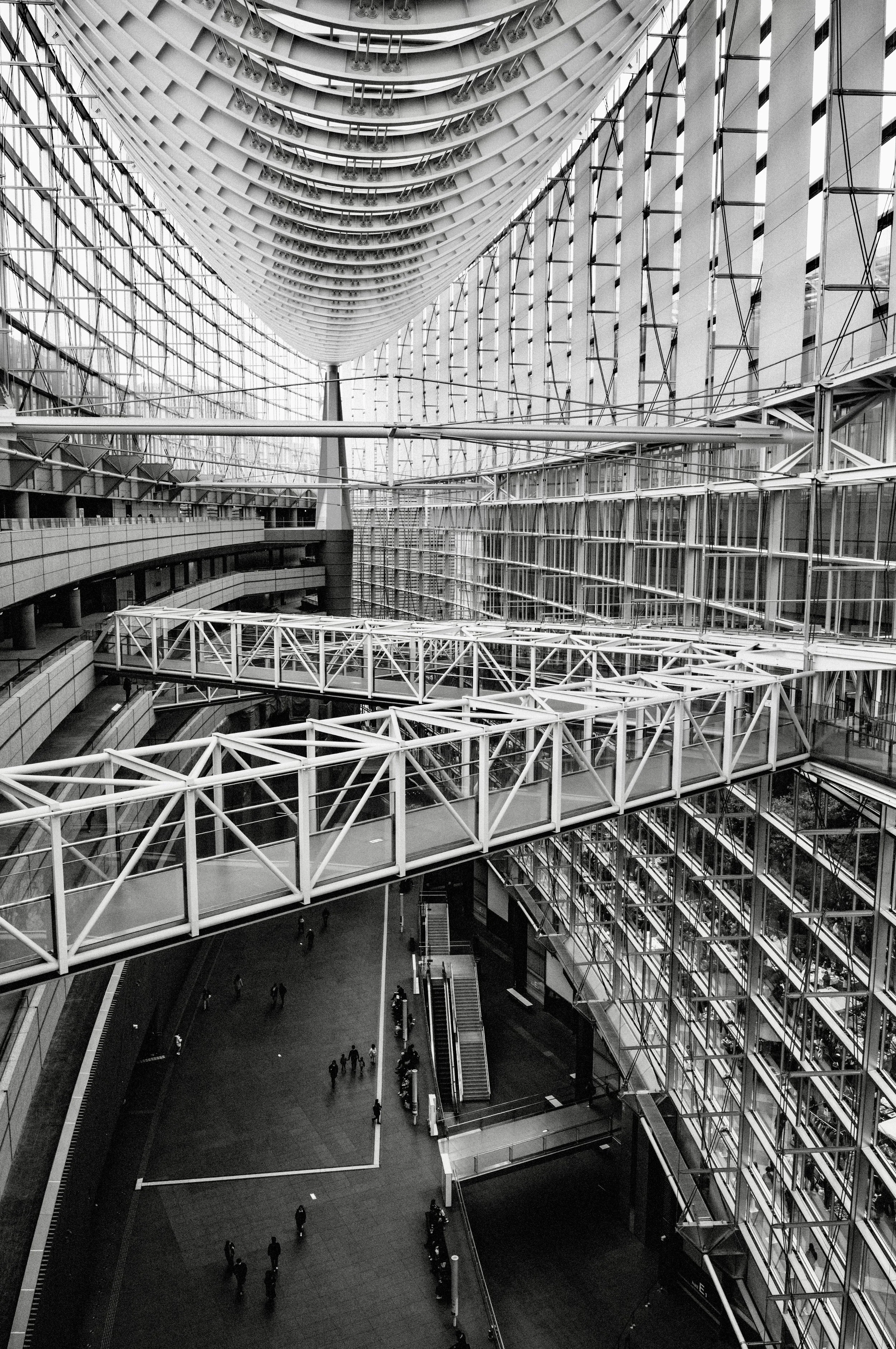 Black and white interior photograph of Tokyo International Forum showing steel walkways, glass walls, and curved architectural lines.