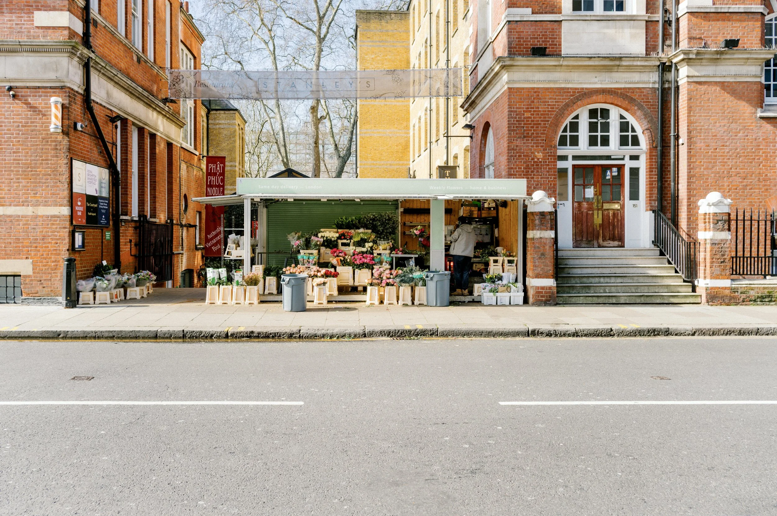 Small flower stall on a quiet Chelsea street in London surrounded by red brick buildings and spring sunlight.
