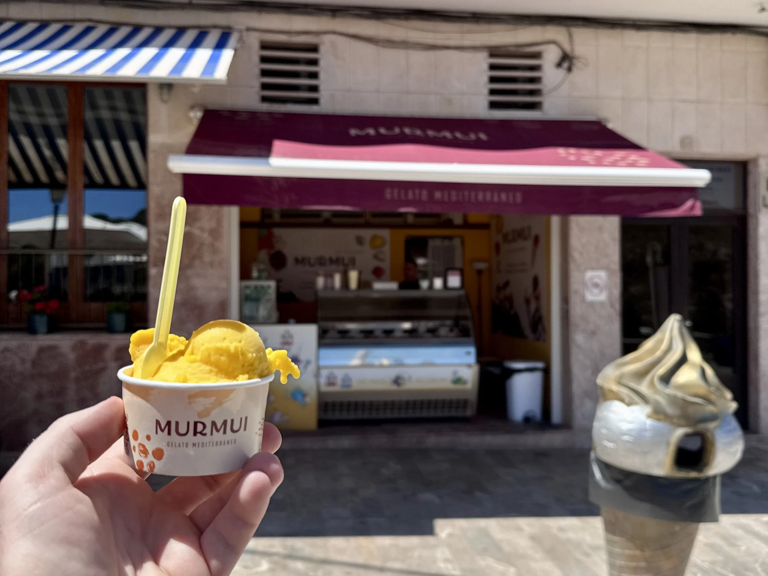 Hand holding a cup of mango sorbet outside the Murmui Gelato Mediterráneo shop in Mallorca