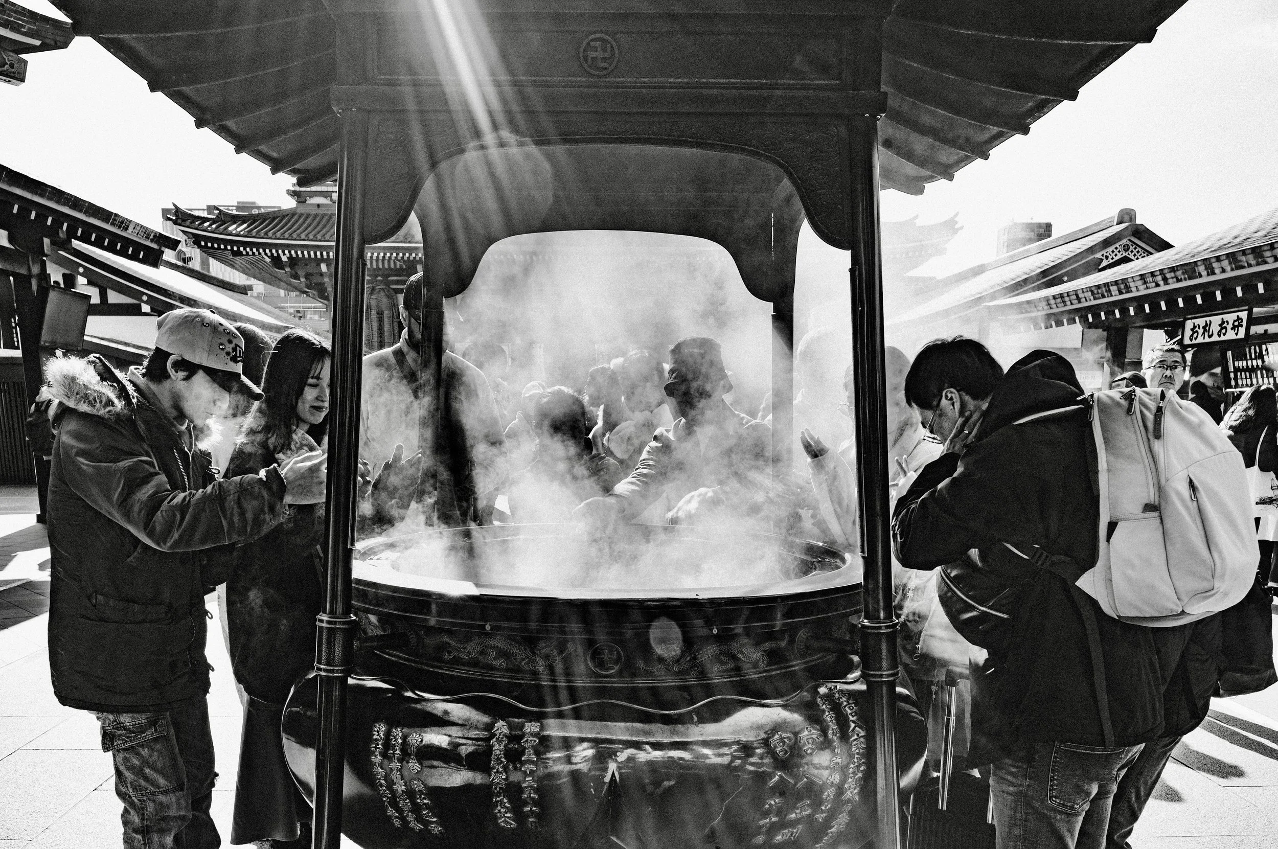 Black and white photograph of visitors gathering around the incense burner at Sensō-ji Temple in Tokyo with sunlight streaming through smoke.