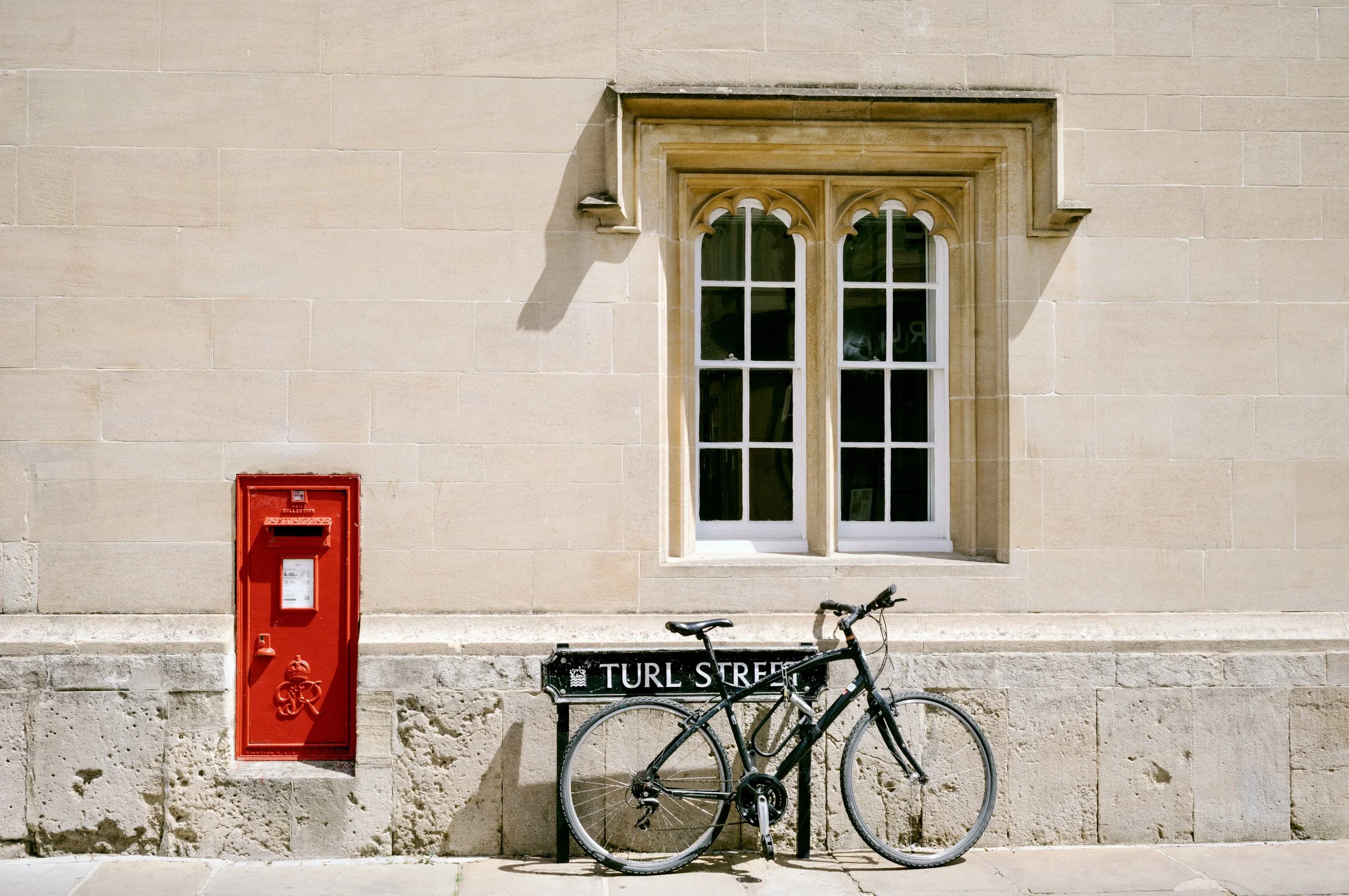 Red Victorian postbox and bicycle against a sandstone college wall on Turl Street, Oxford