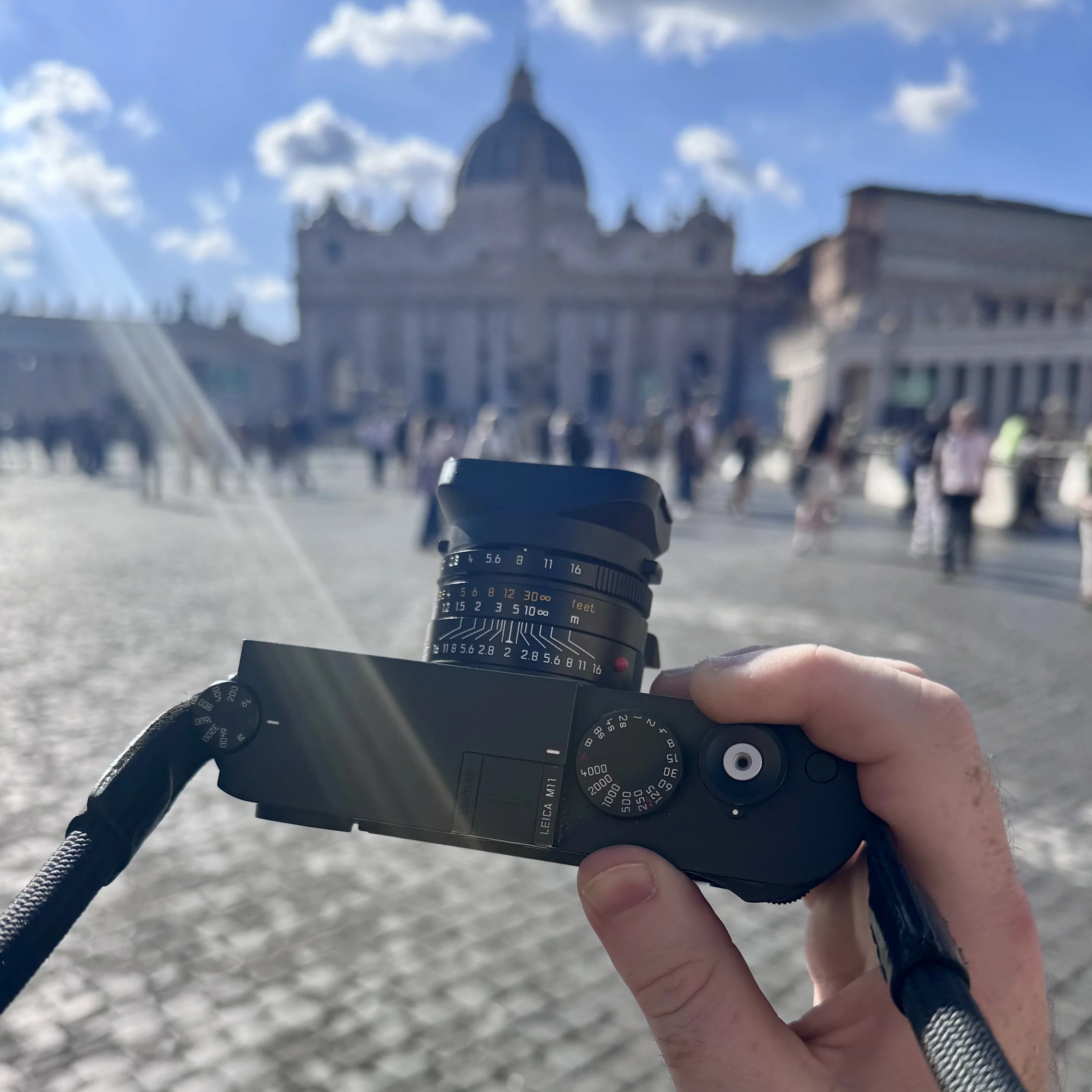 Leica M11 digital rangefinder held up in St Peter's Square, Vatican City, with the basilica dome visible in the background