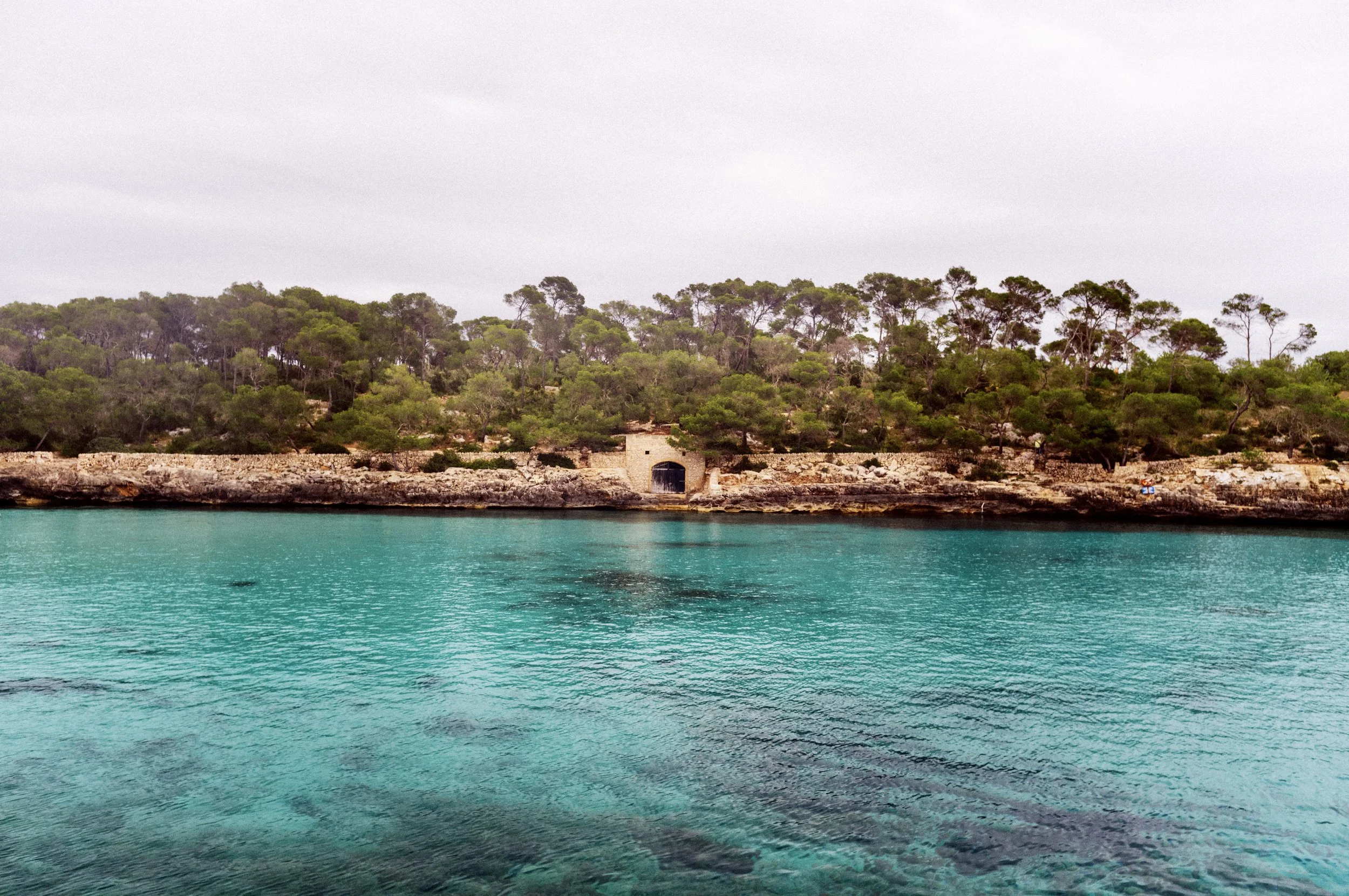 Old stone boat house among pine woods beside a calm turquoise bay at Mondragó, Mallorca