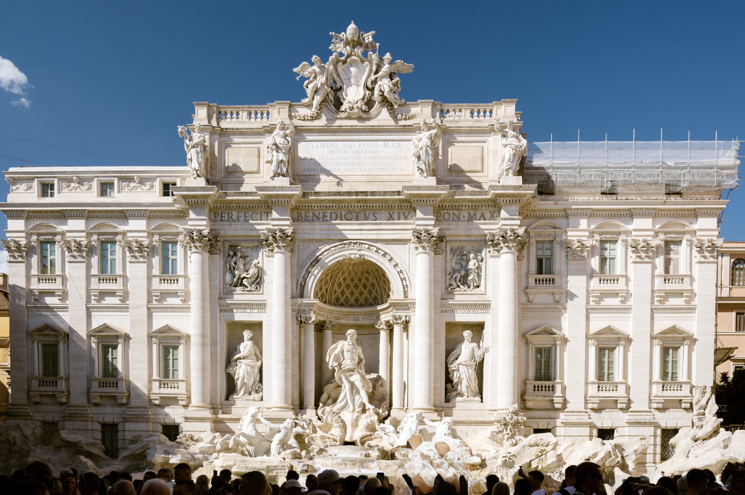 Trevi Fountain in Rome with clear turquoise water, baroque statues, and people tossing coins for good luck.