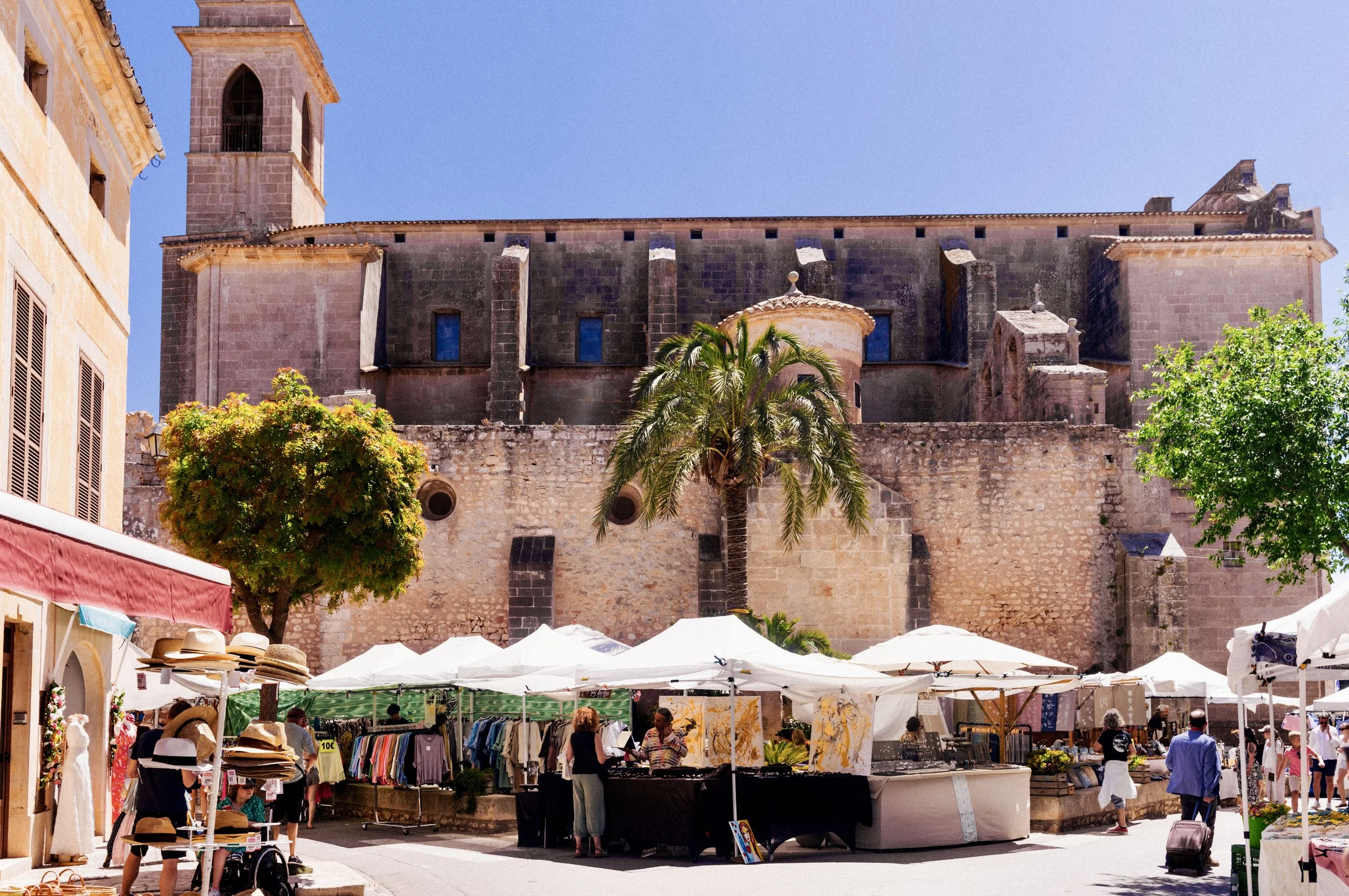 Market stalls and shoppers in front of the historic stone church in Santanyí, Mallorca